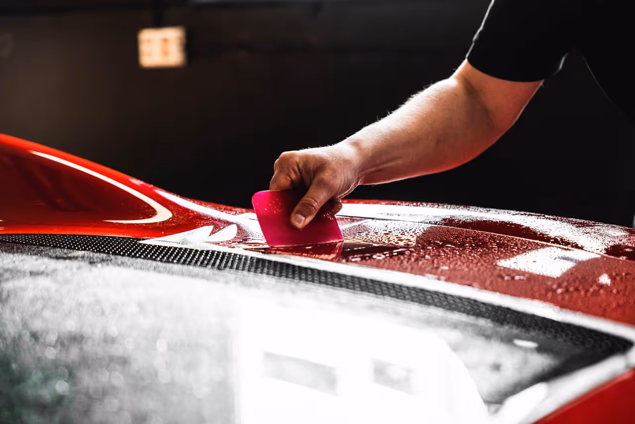 En person bruker et rosa verktøy til å påføre eller fjerne folie på en våt, rød bil.