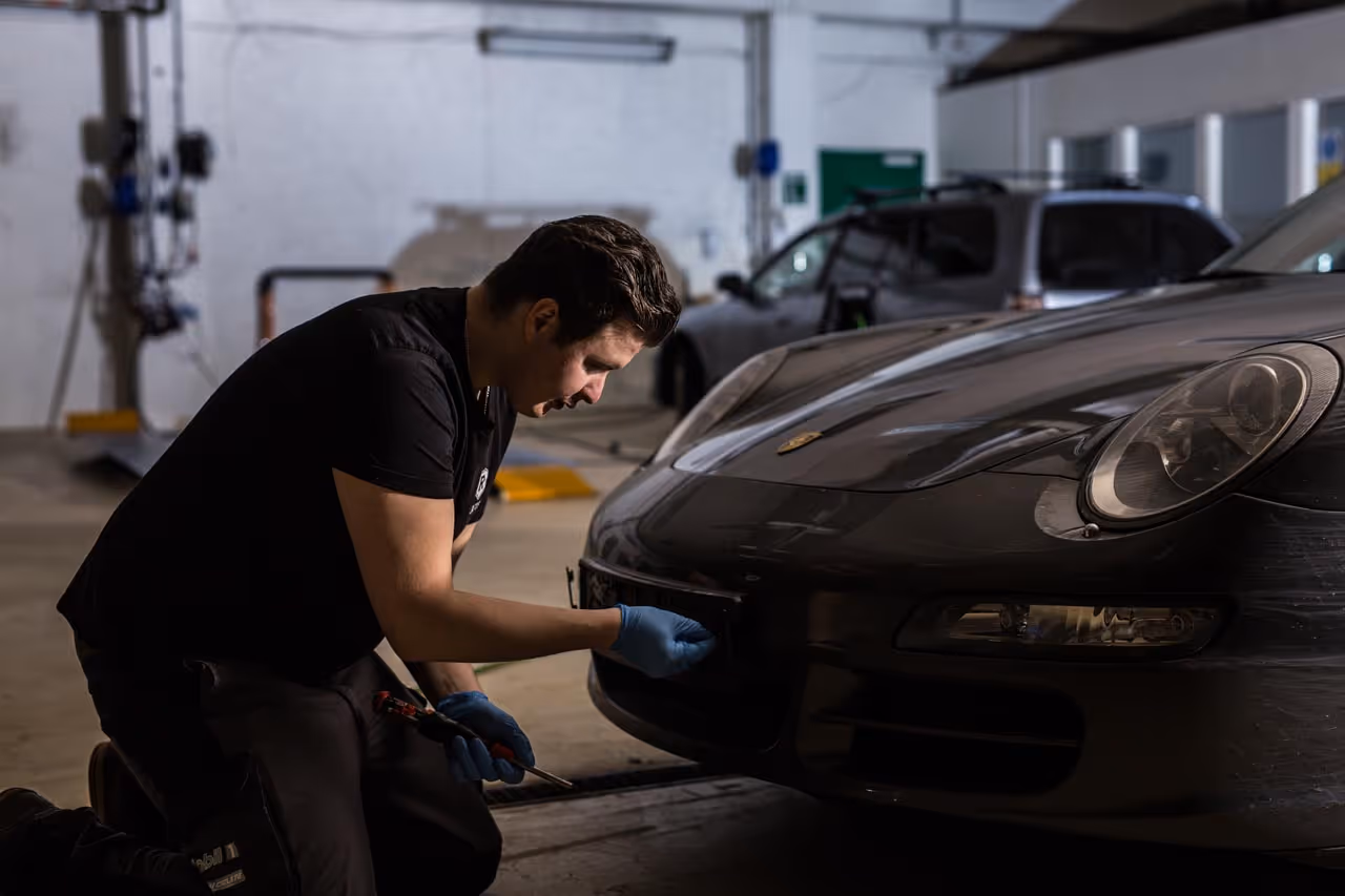 Mekaniker som jobber på fronten av en svart Porsche i et verksted.