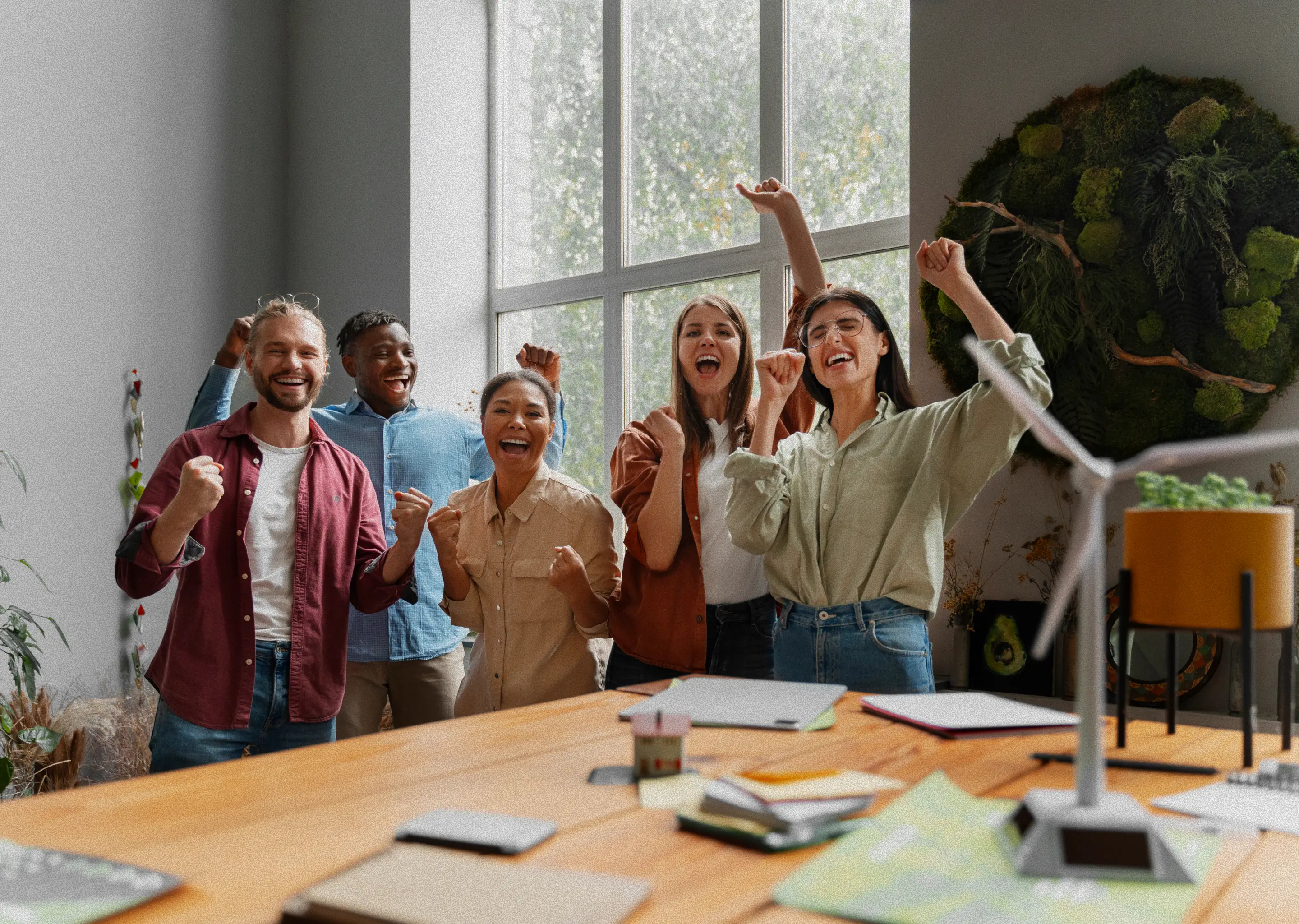 A low-angle shot shows a diverse group of five smiling colleagues, three women and two men, standing and cheering with their fists raised in the air.