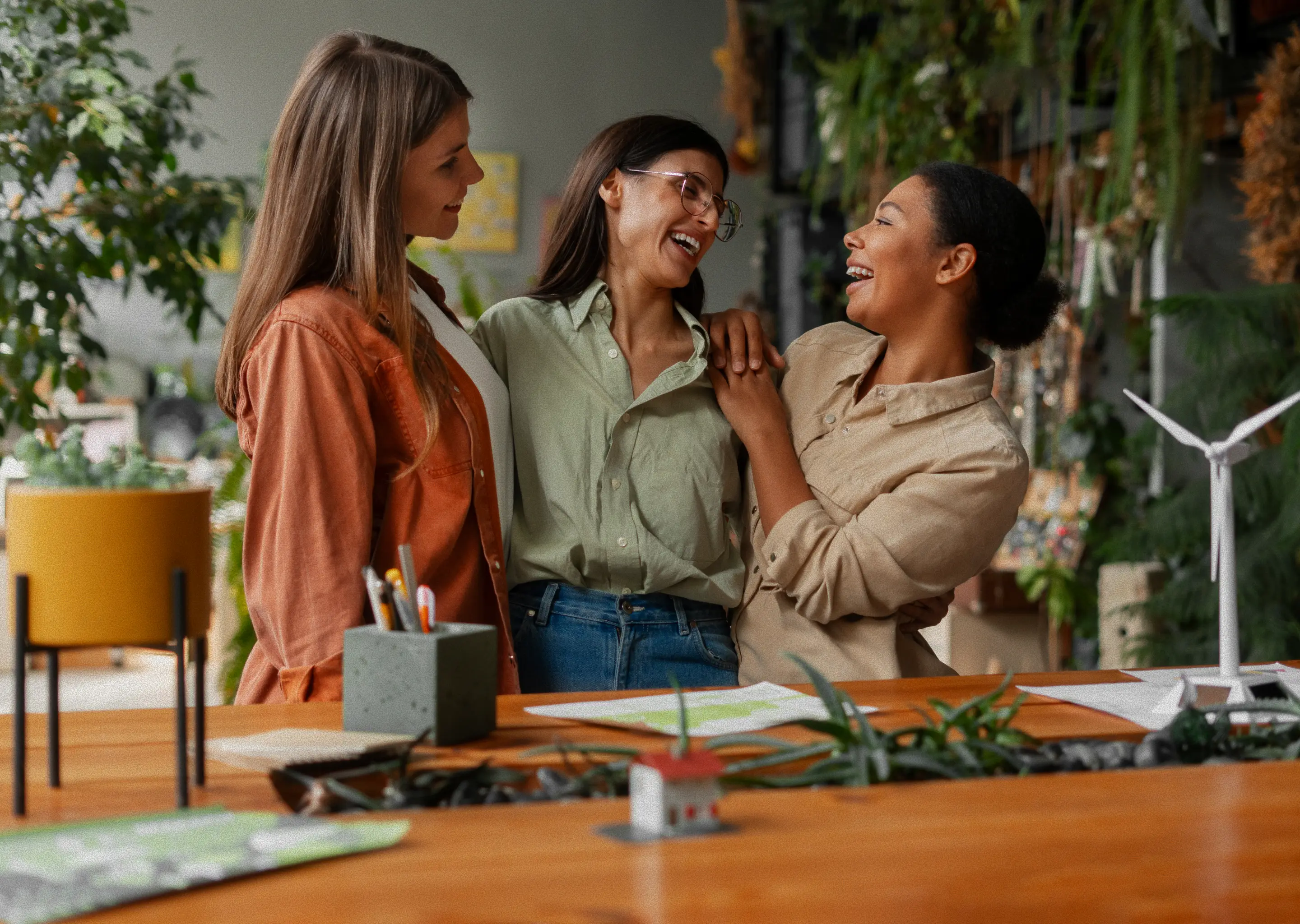 Three friends laughing together at a classroom table, showing friendship and connection.