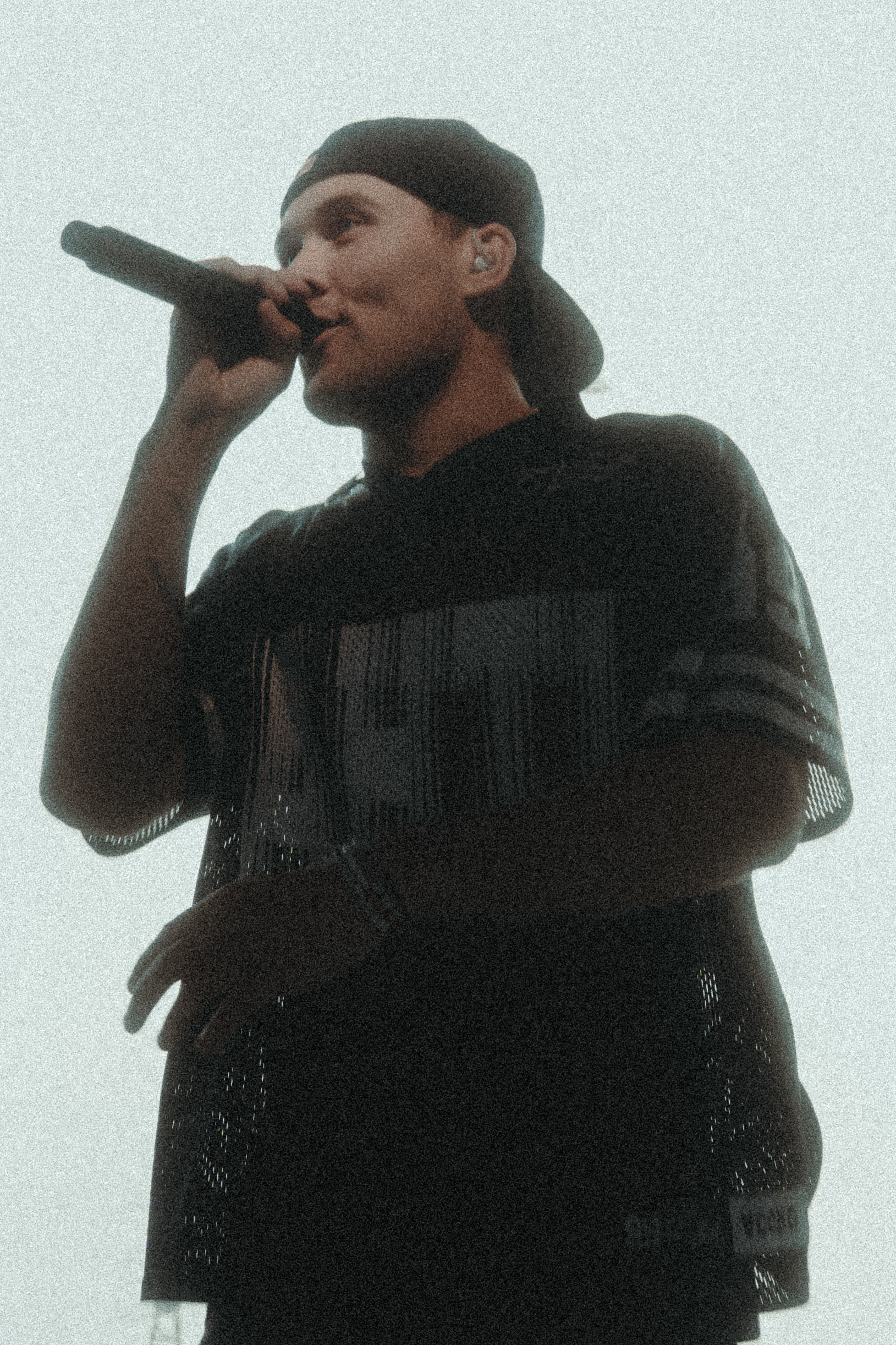 Man wearing a backward cap singing into a microphone with a light background.