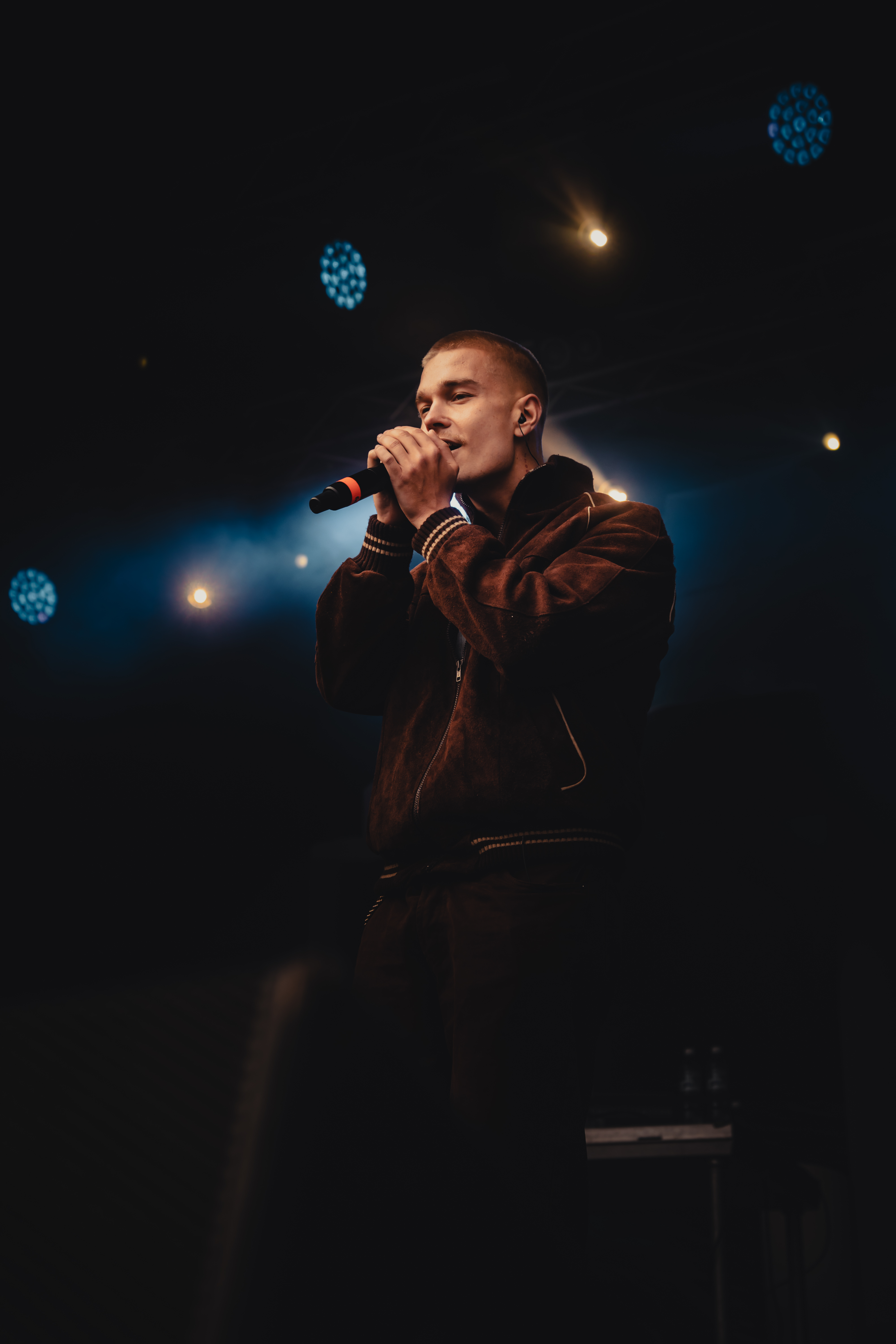 Male singer performing on stage holding a microphone with stage lights in the background.