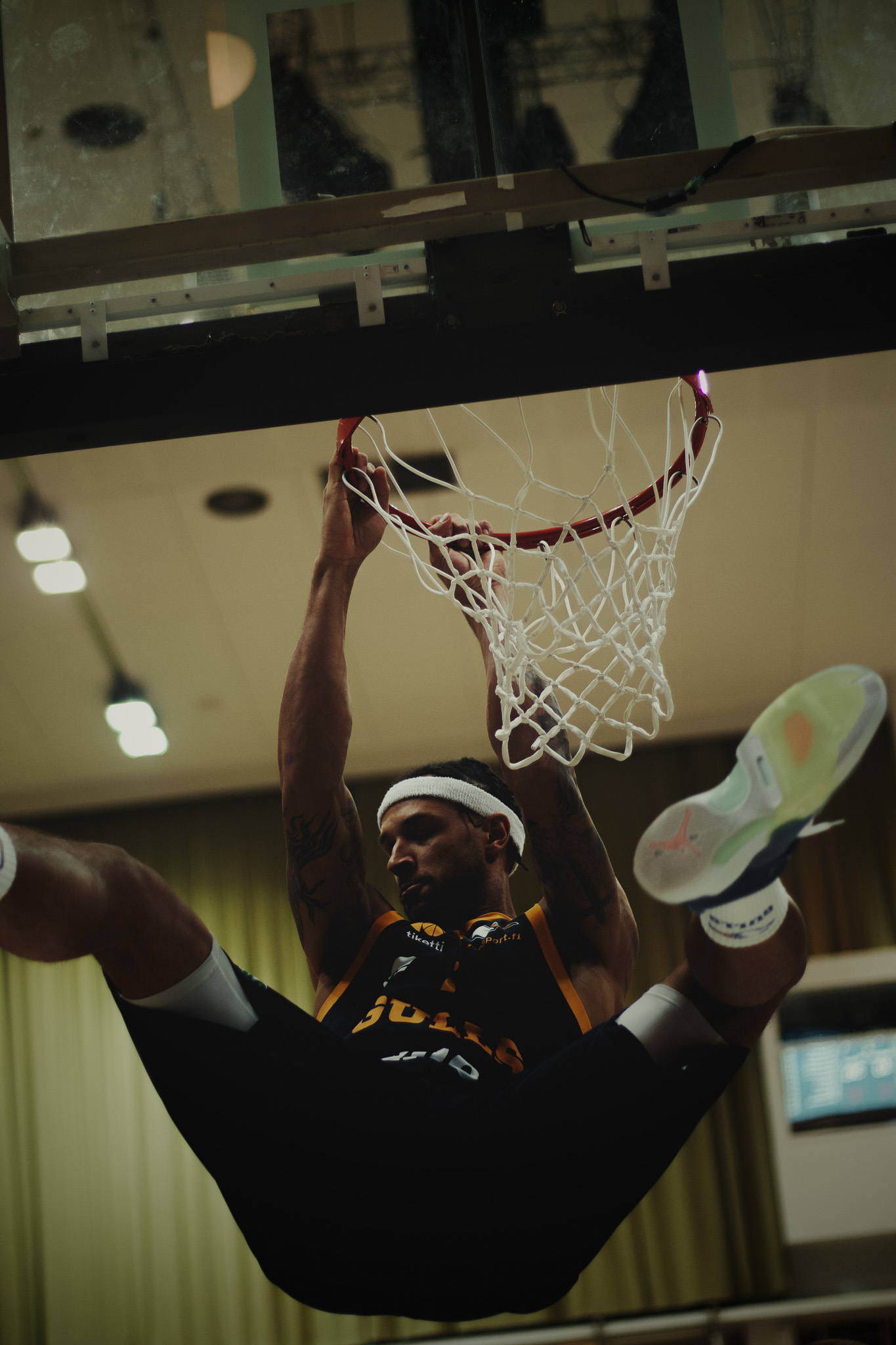 Basketball player hanging from the rim after a slam dunk inside an indoor court.