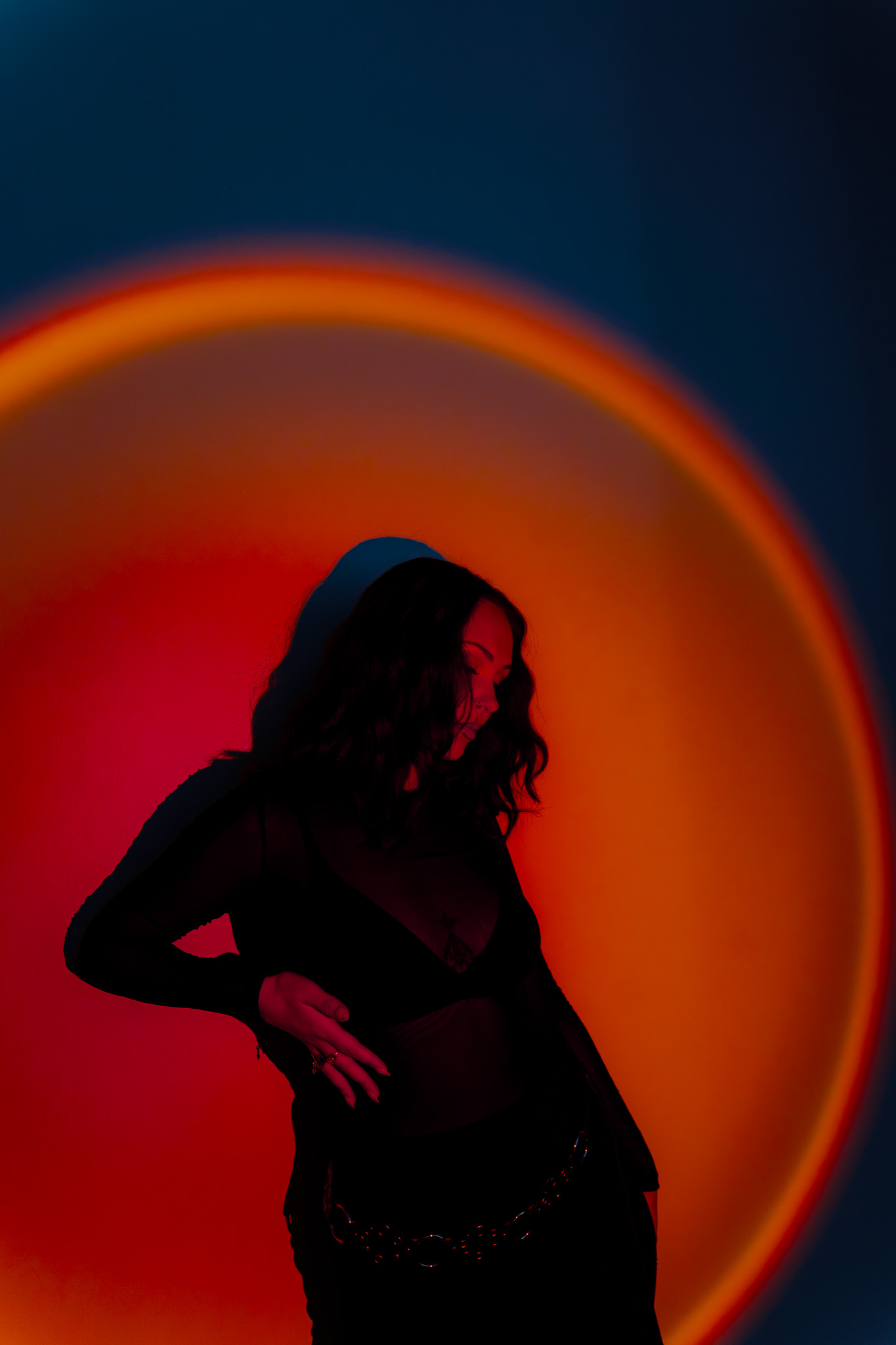 Woman with dark curly hair posing against a background lit with red and orange circular lighting.