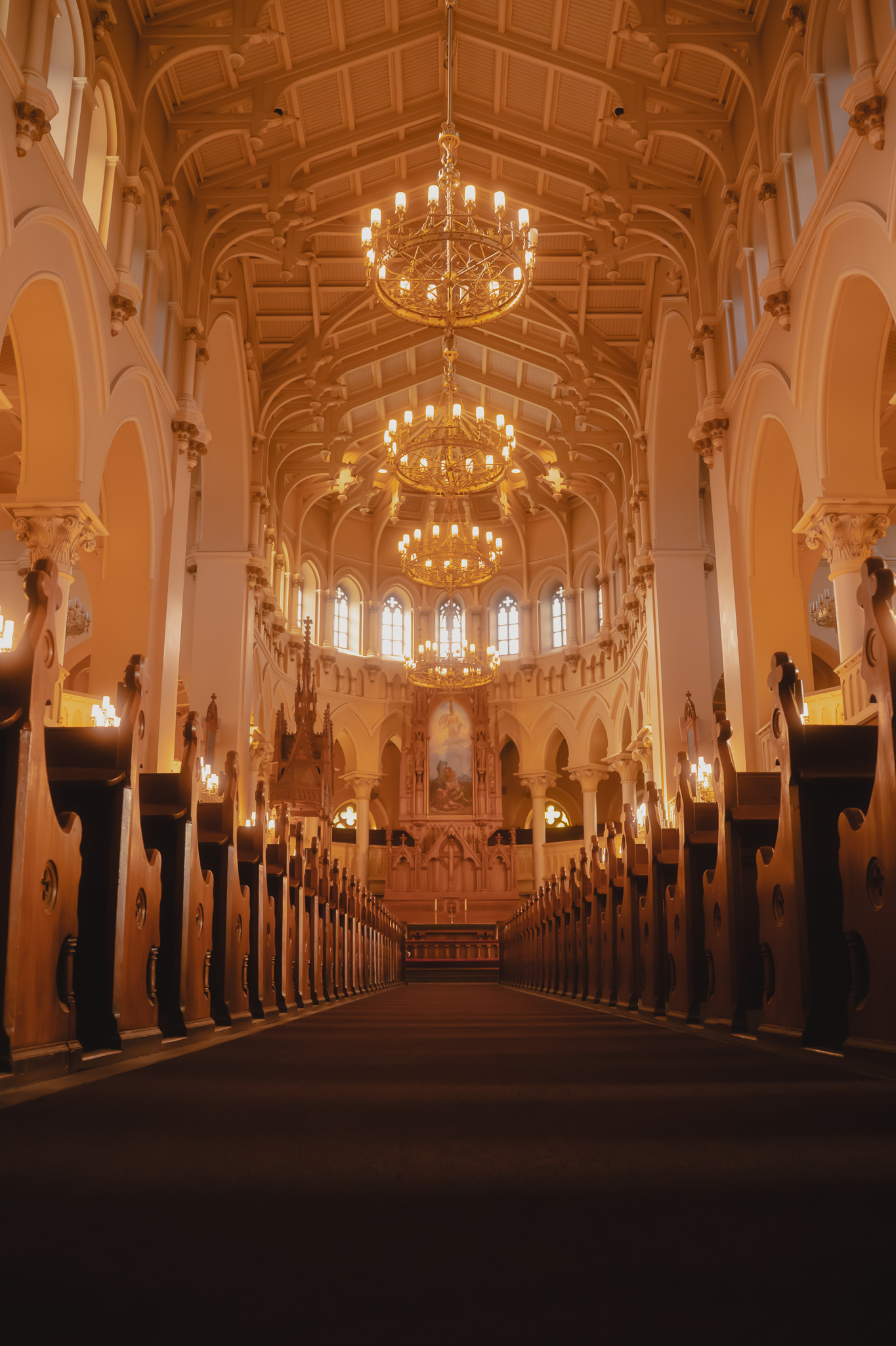 Interior of a grand church with tall wooden pews, ornate chandeliers, and a decorated altar under a vaulted ceiling.