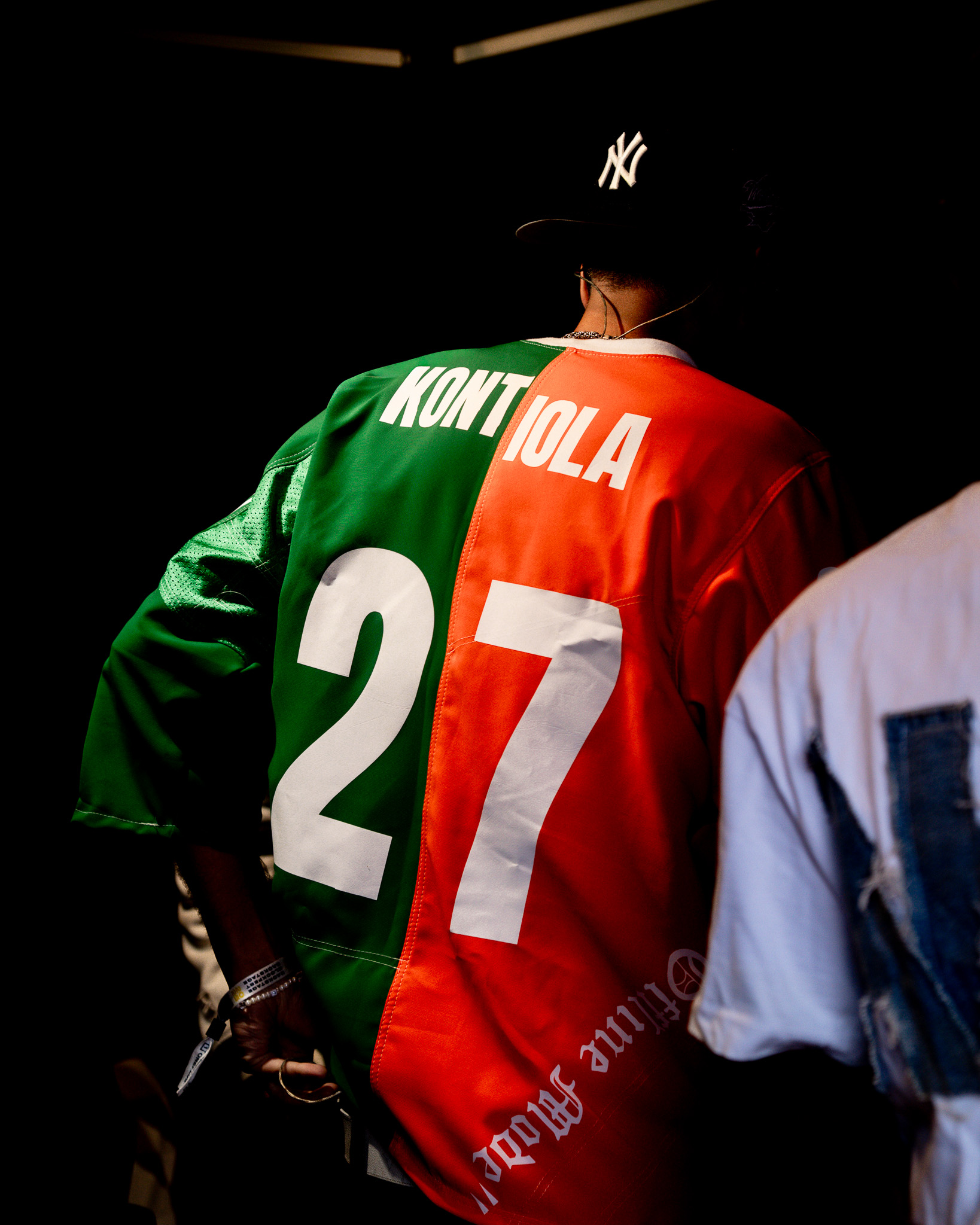 Person wearing a green and orange jacket with the name 'KONTIOLA' and number 27 on the back, and a black New York Yankees cap.