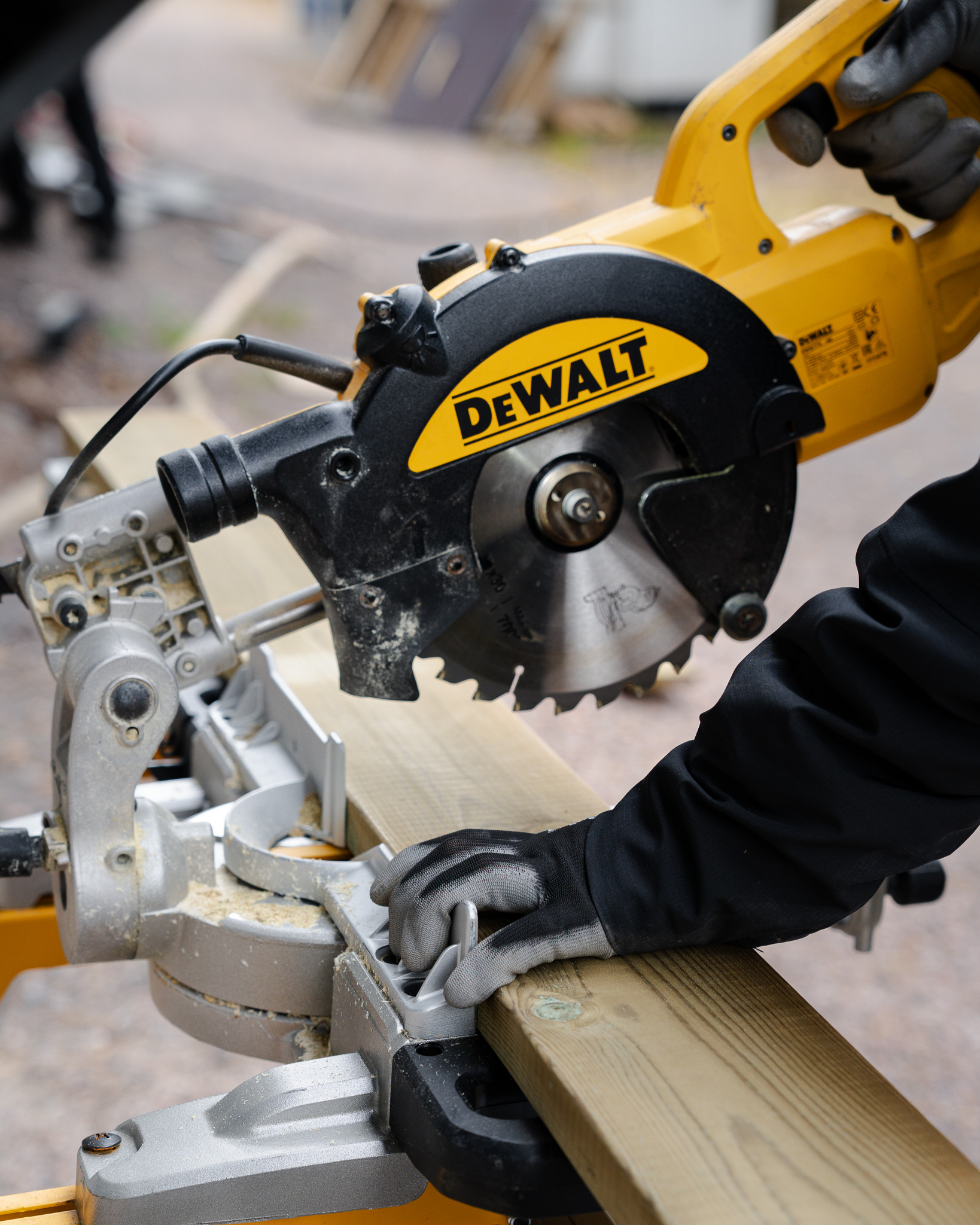 Person wearing gloves operating a yellow DeWalt miter saw cutting a wooden plank.