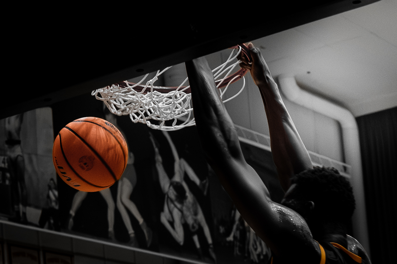 Basketball player dunking the ball into the hoop with the ball mid-air near the net.