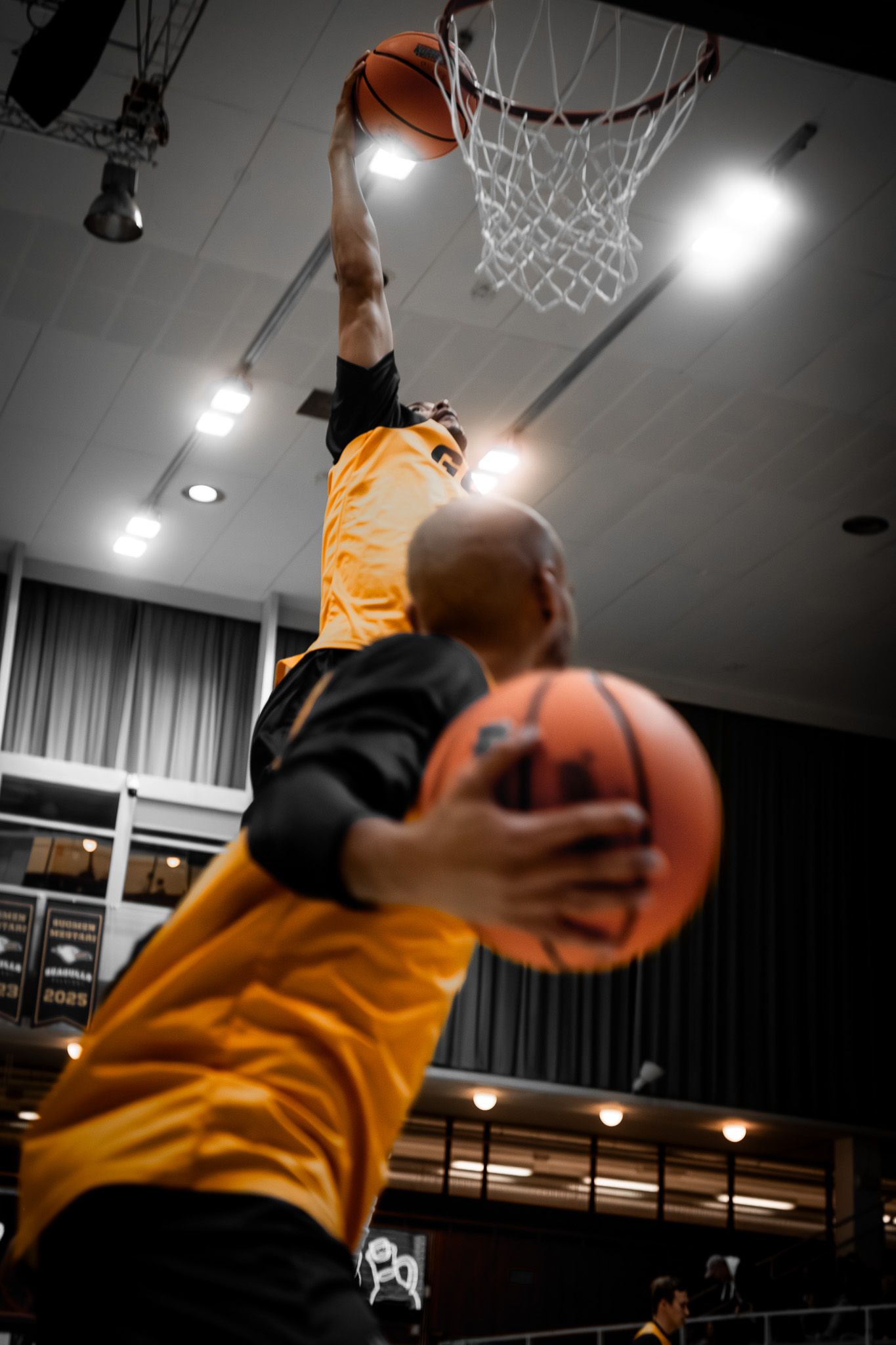 Two basketball players in yellow jerseys competing near the hoop in an indoor gym.