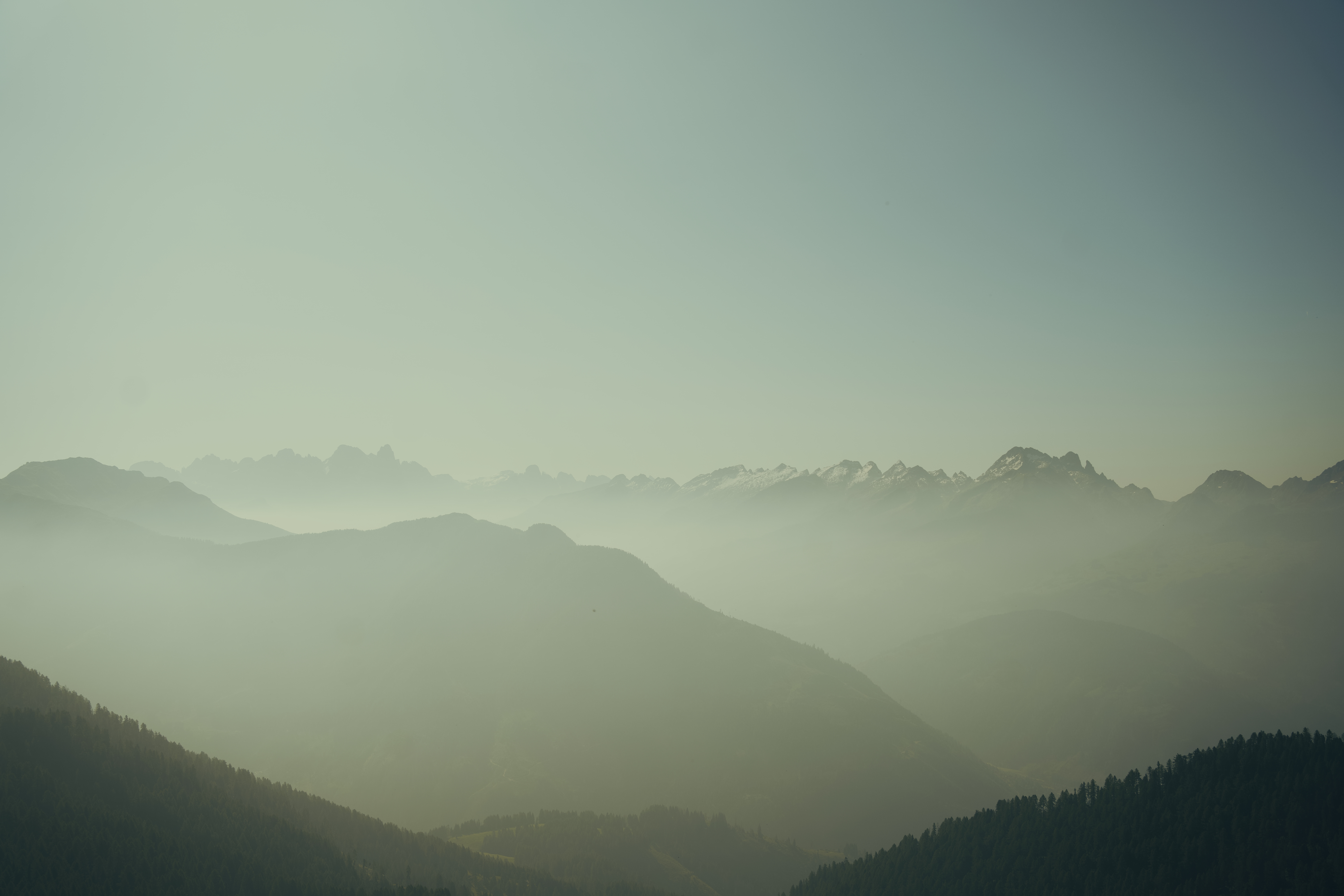 Layers of mist-covered mountains under a clear pale sky.