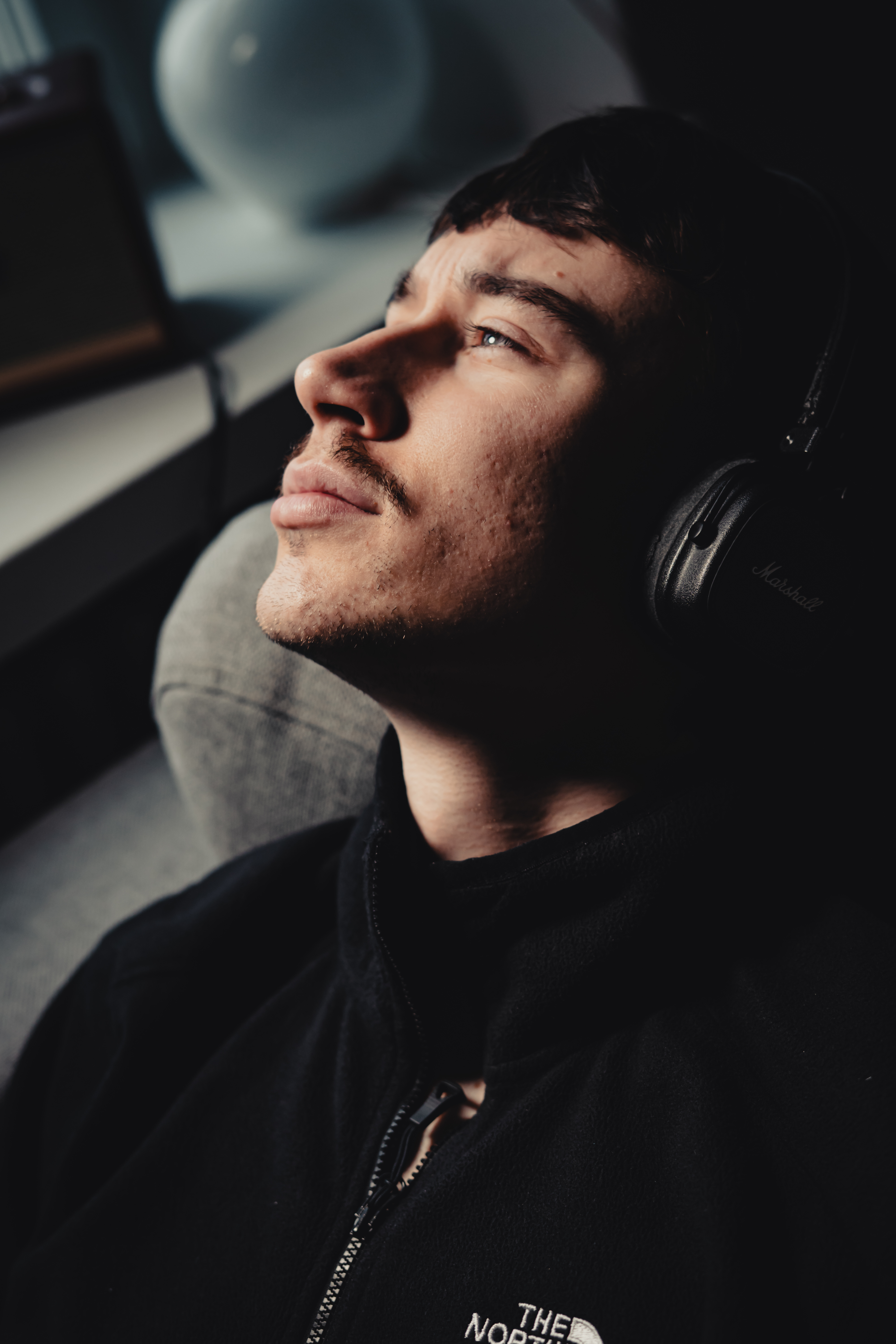 Young man with headphones gazing upward while seated indoors near a window.