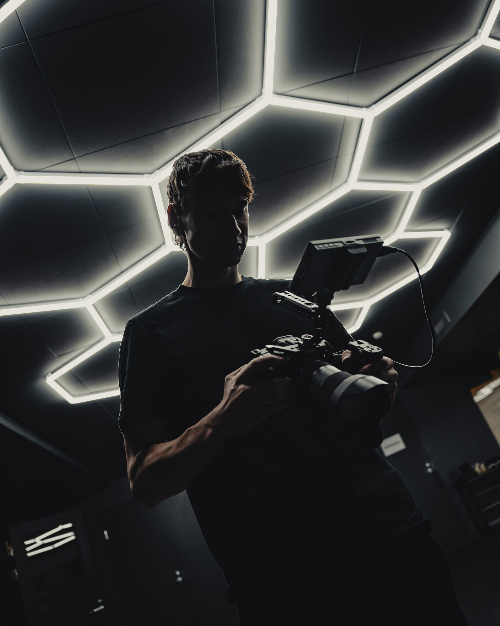 Silhouetted person holding a professional camera with a large lens under geometric LED ceiling lights.