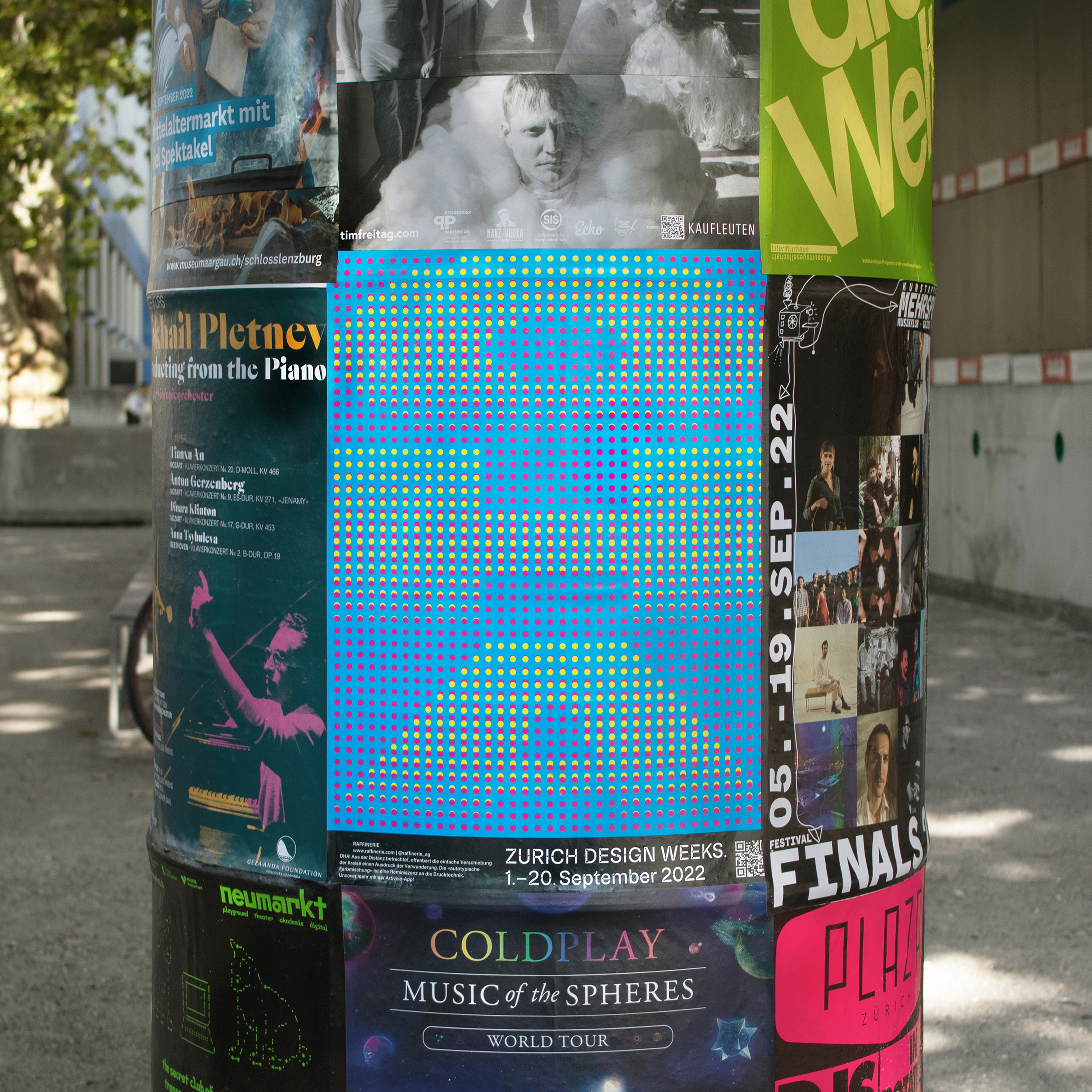Close up of A2 Poster of the word OHA in Cyan, Magenta, and Yellow hanging on a pillar on the streets of altstetten