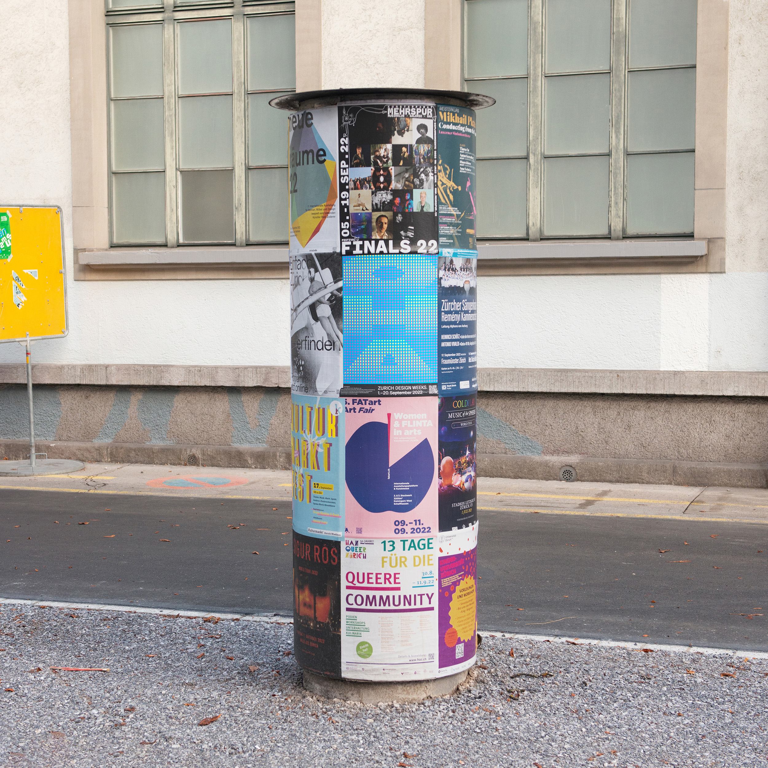 A2 Poster of the word OHA in Cyan, Magenta, and Yellow hanging on a pillar on the streets of zurich