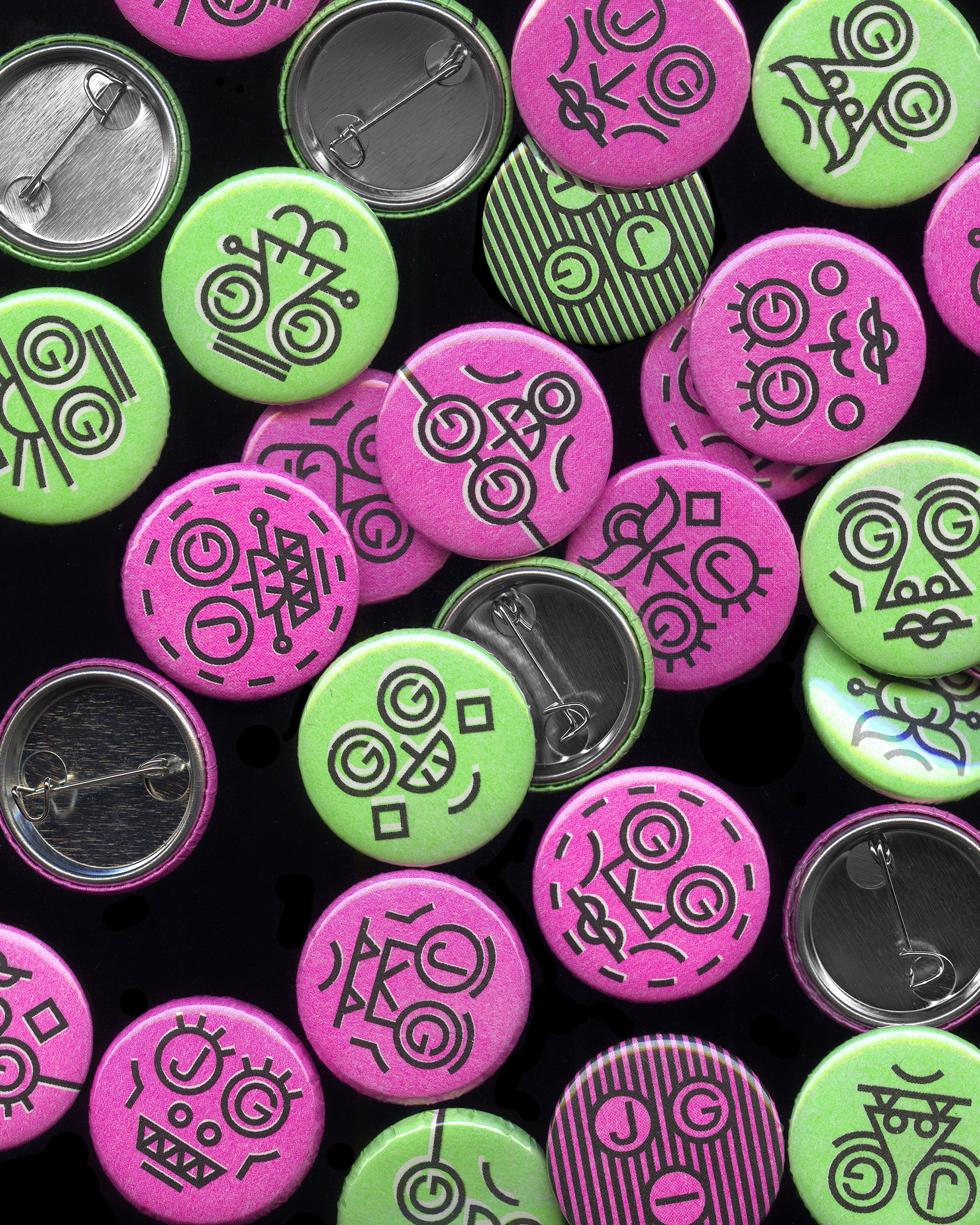 Collection of green and pink round pin-back buttons with abstract black face designs on a black background.
