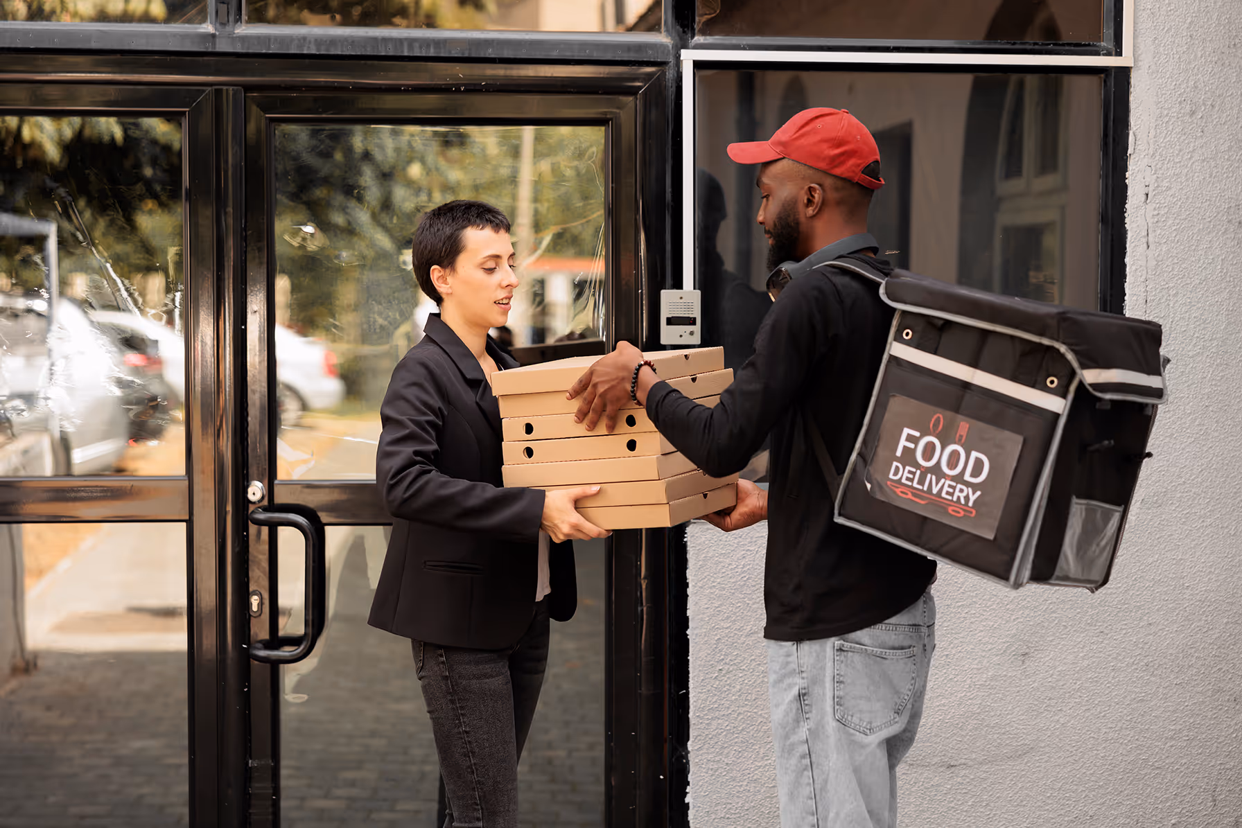 Delivery driver with a delivery backpack handing over Pizza Boxes to a women in front of a building