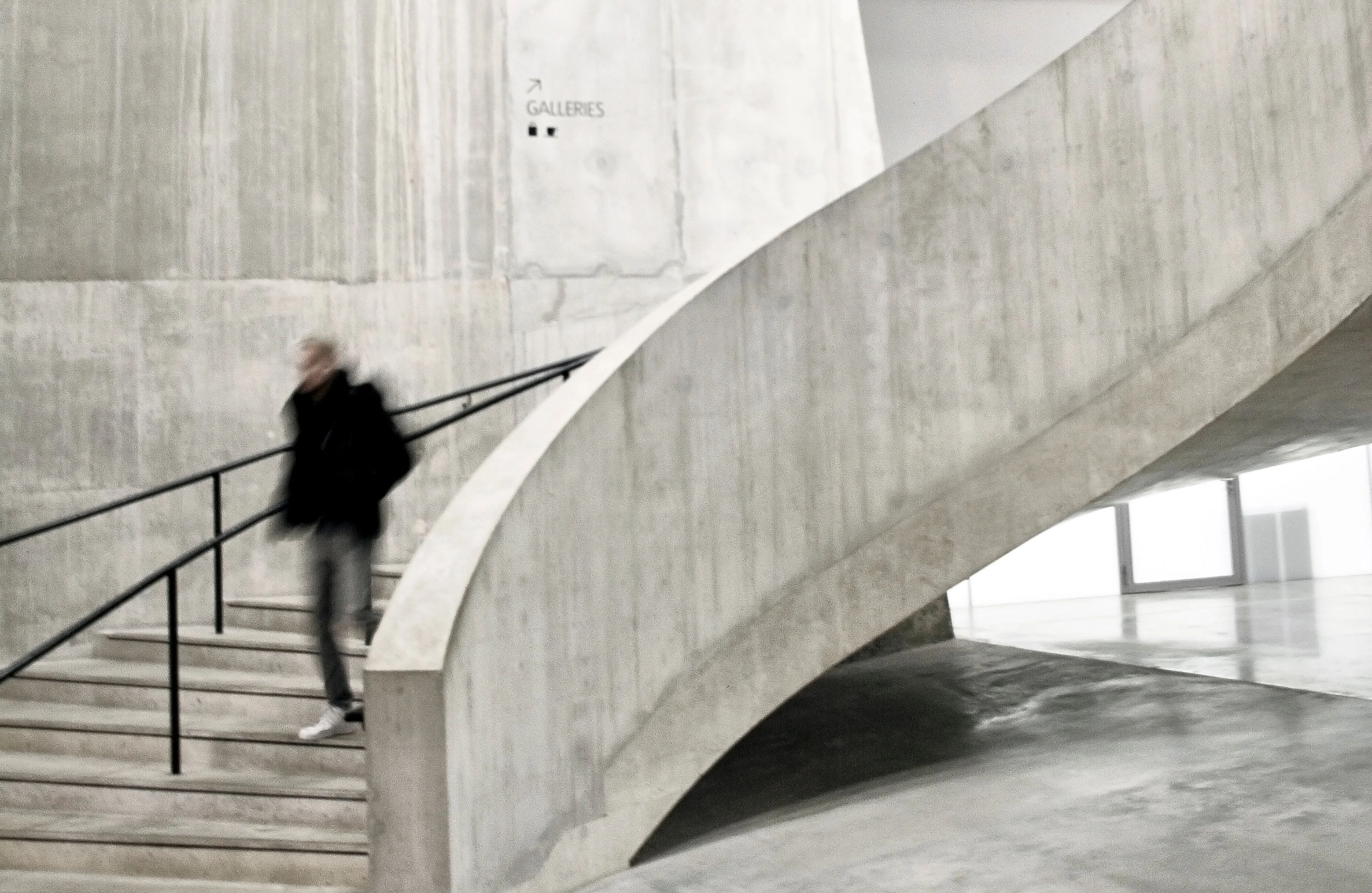 A modern architectural interior featuring a concrete spiral staircase with a blurred figure in motion