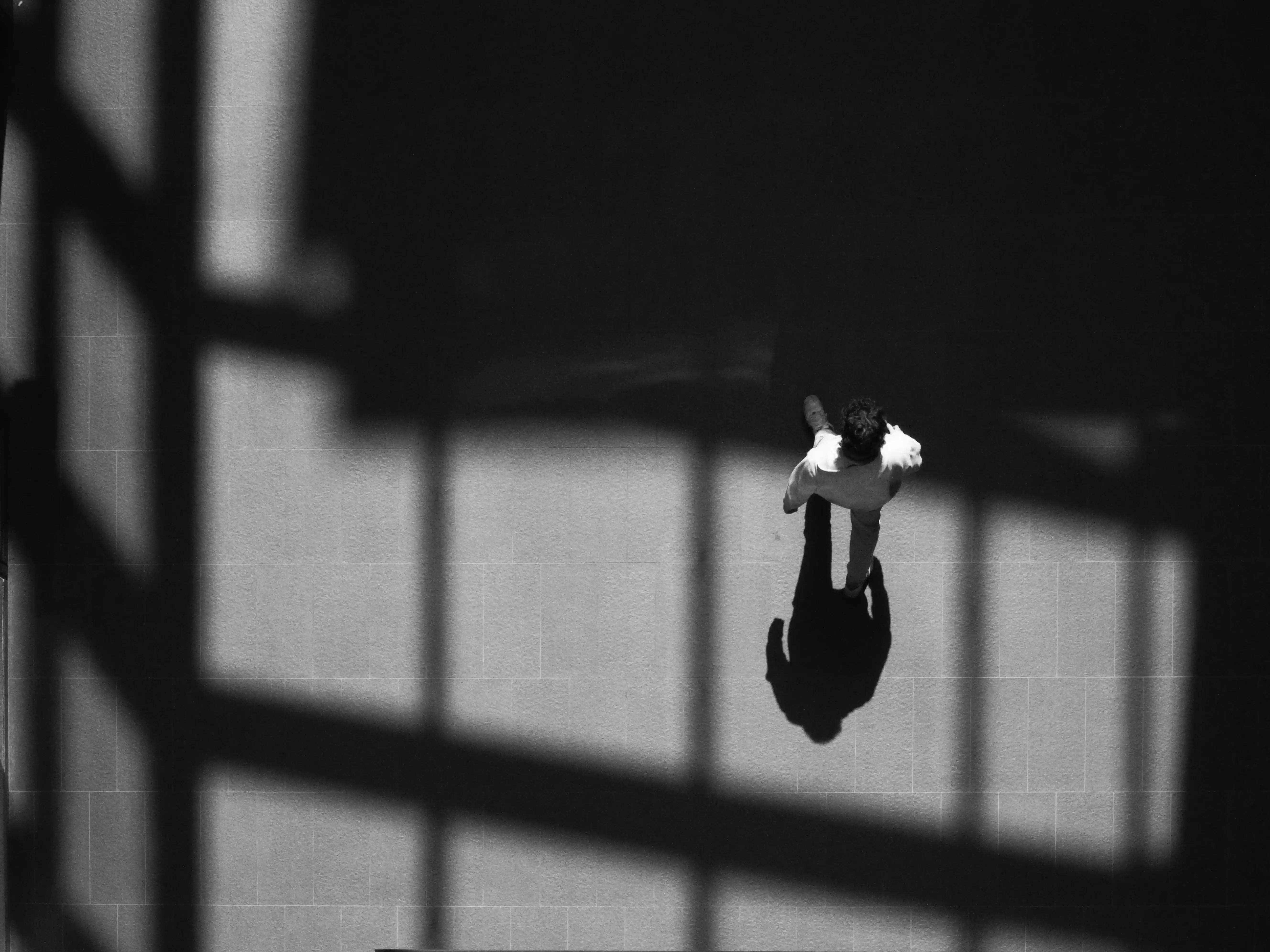 Person navigating a built environment through architectural shadows and spatial cues