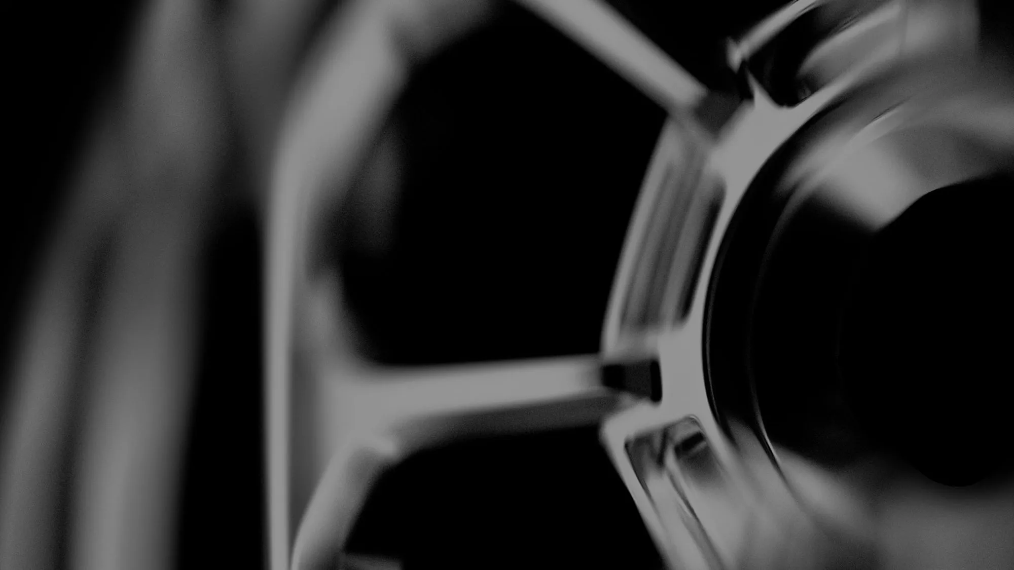 Close-up, abstract black and white image of a metallic wheel rim with spokes.