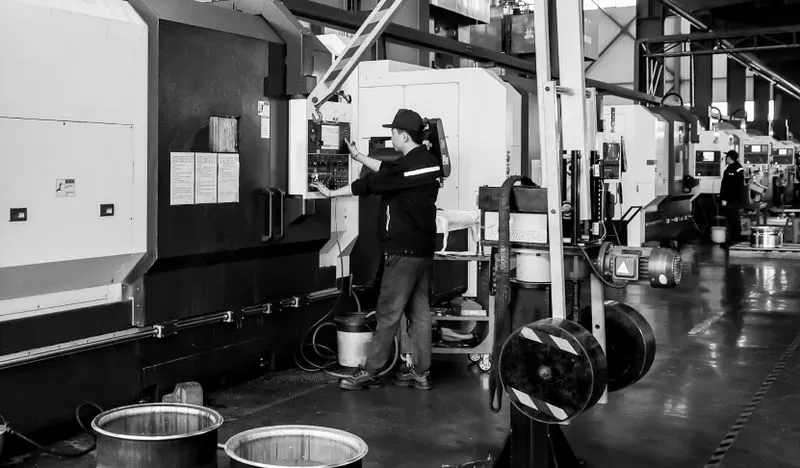 Worker operating a CNC milling machine inside a factory with multiple machines and metal containers on the floor.