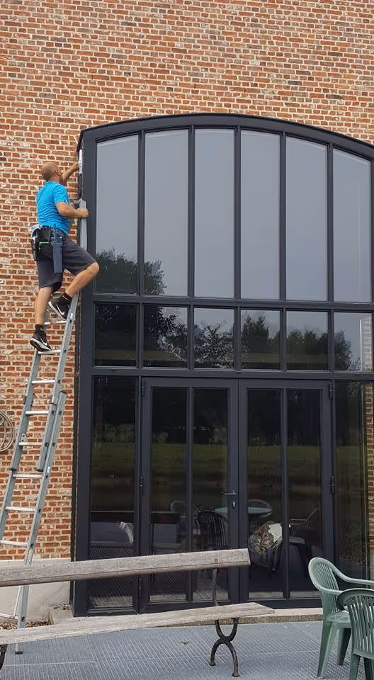 Professionele ramenwasser op ladder reinigt hoge glaspartijen bij bedrijf in Schoten