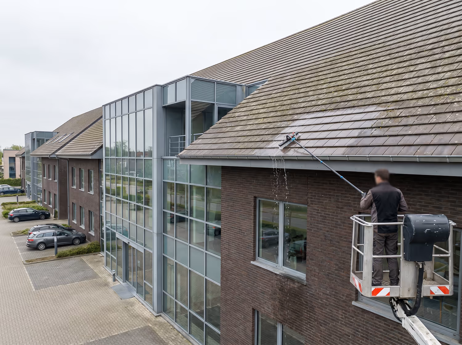 Man op een hefplatform die een dak schoonmaakt met een lang borstelsysteem.