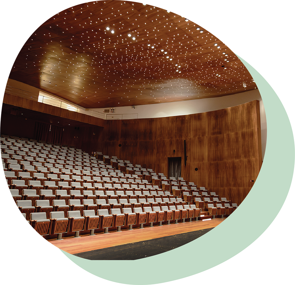 Oval shape image showing Forum Bertarelli concert hall with wooden walls and ceiling featuring star-like lights, empty blue seats, and a grand piano on stage.