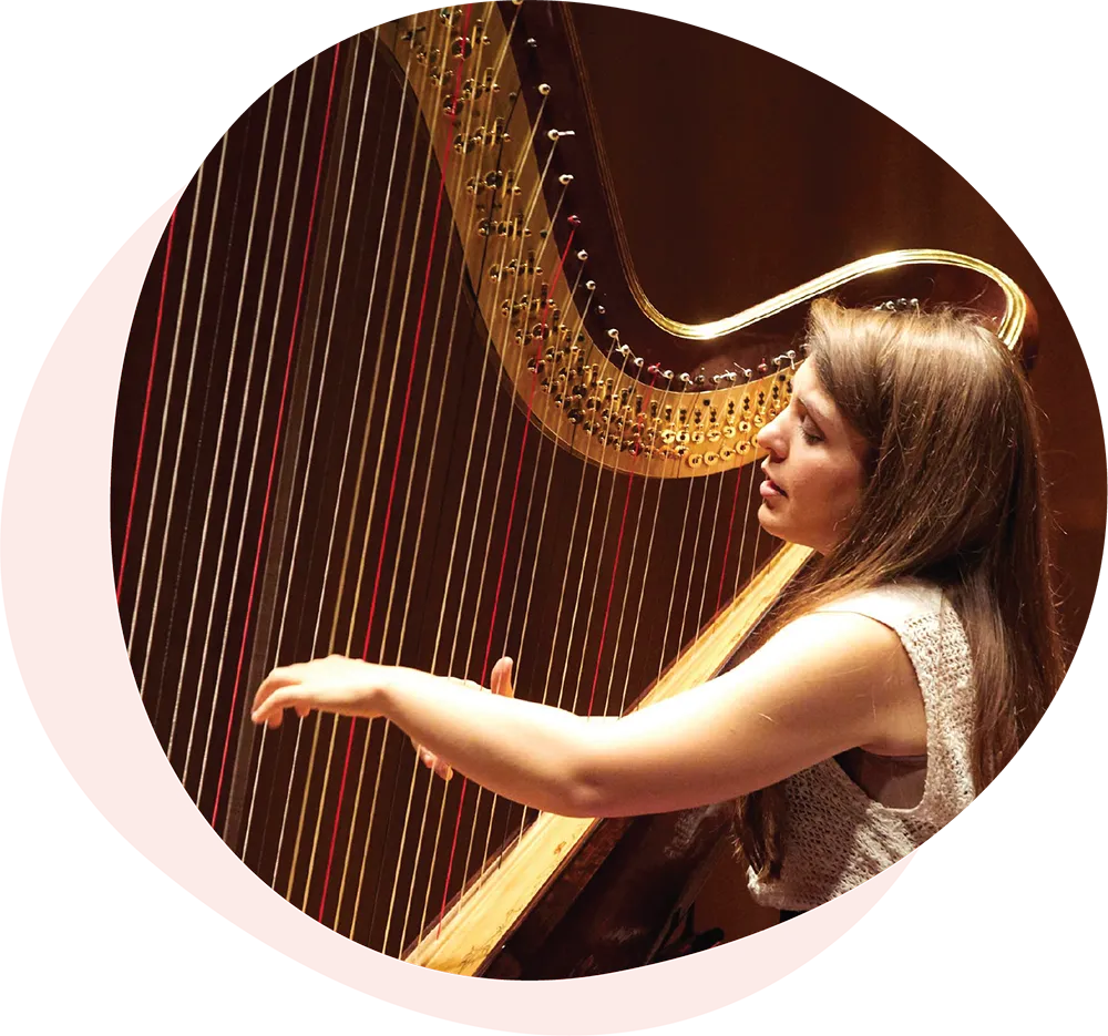 Woman playing a large wooden harp with focused expression.