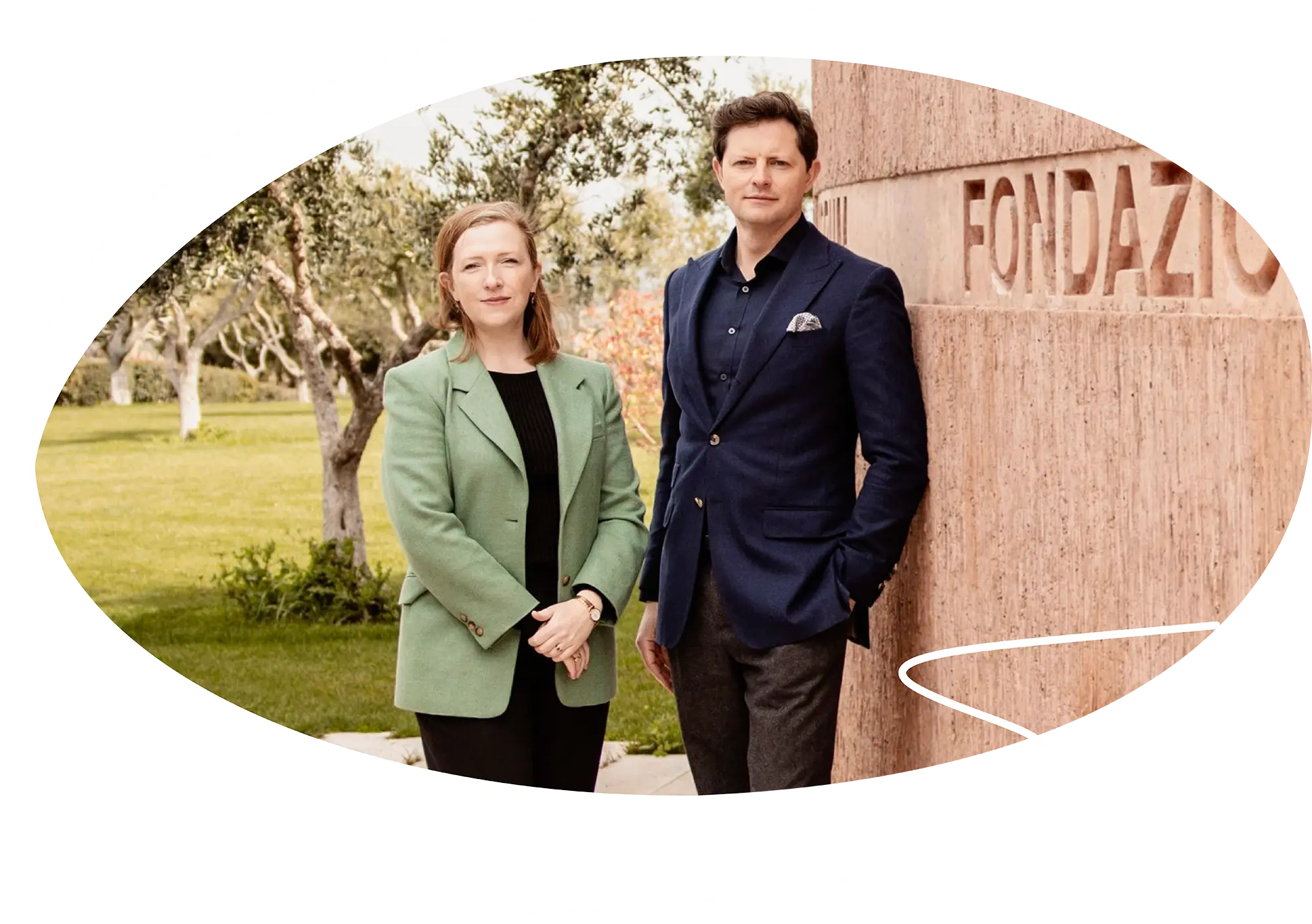 Nicholas Chalmers talking and with Rosenna East, standing outdoors near a stone balustrade with greenery and flowers.