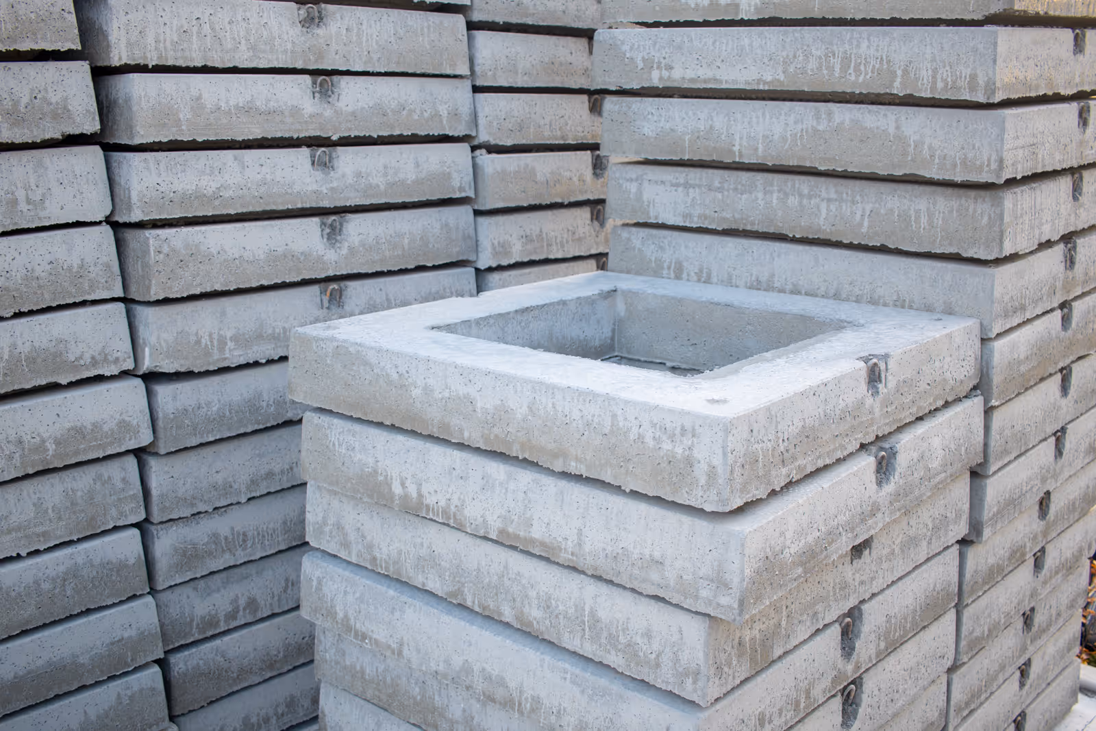 Dekplaat in gewapend beton, met vierkante mangatopening en ingegoten gietijzeren deksel, klaar voor plaatsing op regenput