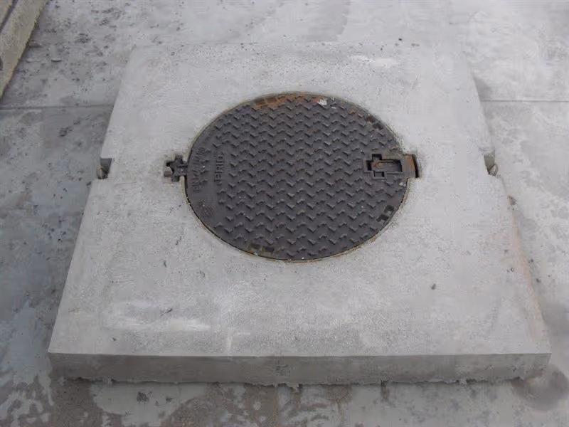 Dekplaat in gewapend beton, met ronde mangatopening en ingegoten gietijzeren deksel, klaar voor plaatsing op regenput