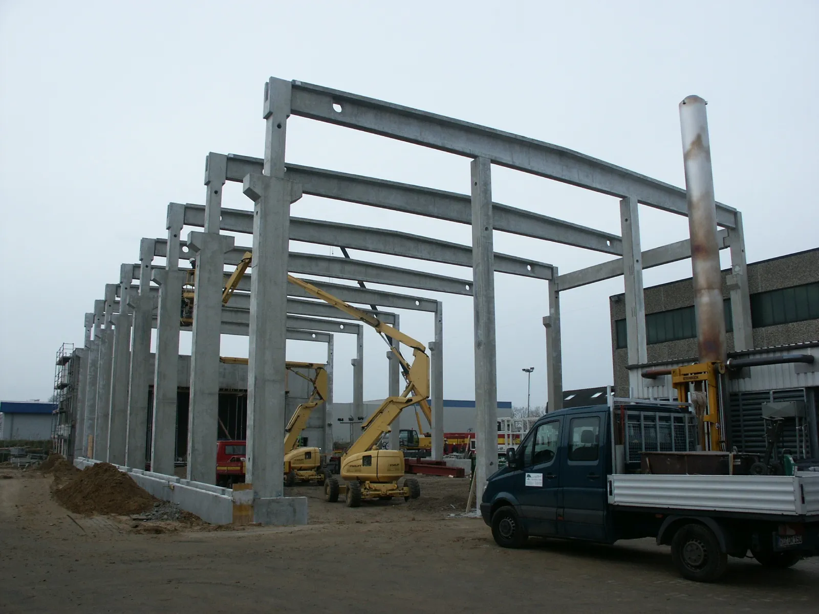 Baustelle mit Stahlrahmenkonstruktion und Hebebühnenfahrzeugen im Gewerbebau.