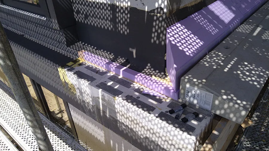 Betonsockel mit Markierungen und Schatten eines Gitters auf einer Baustelle im Sonnenlicht.