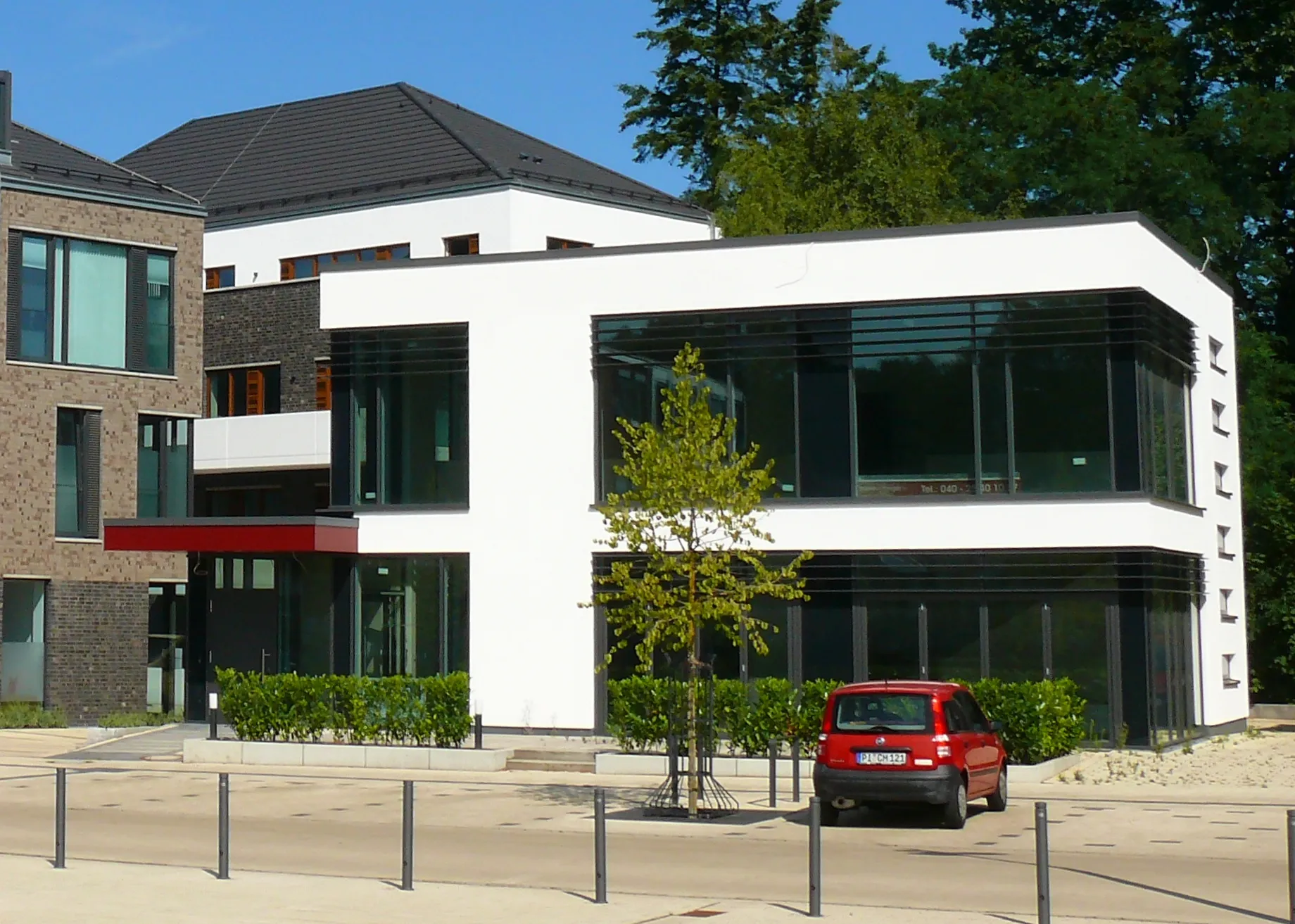 Modern white two-story building with large windows and a red car parked in front under a clear sky.