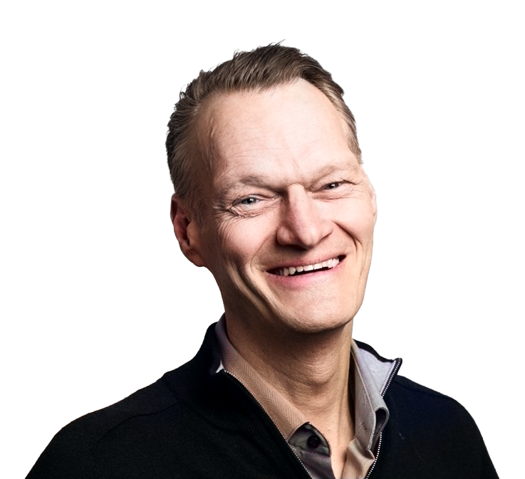 Smilende eldre mann med kort hår iført en svart genser over en brun skjorte med knapp.