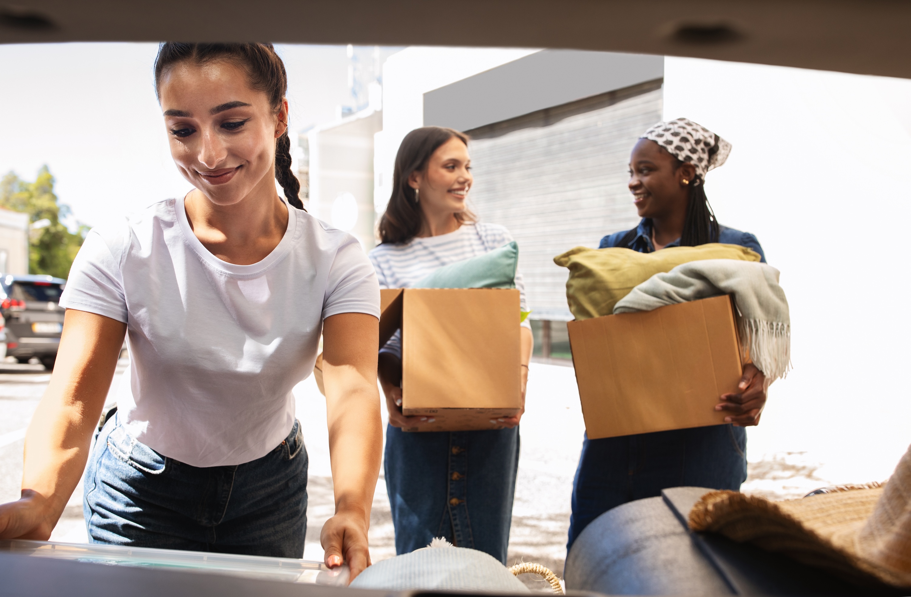 A group of three female roommates smiling while loading moving boxes into a car, representing the smooth move-in process and community at ArtHaus Dwight in Berkeley, CA.