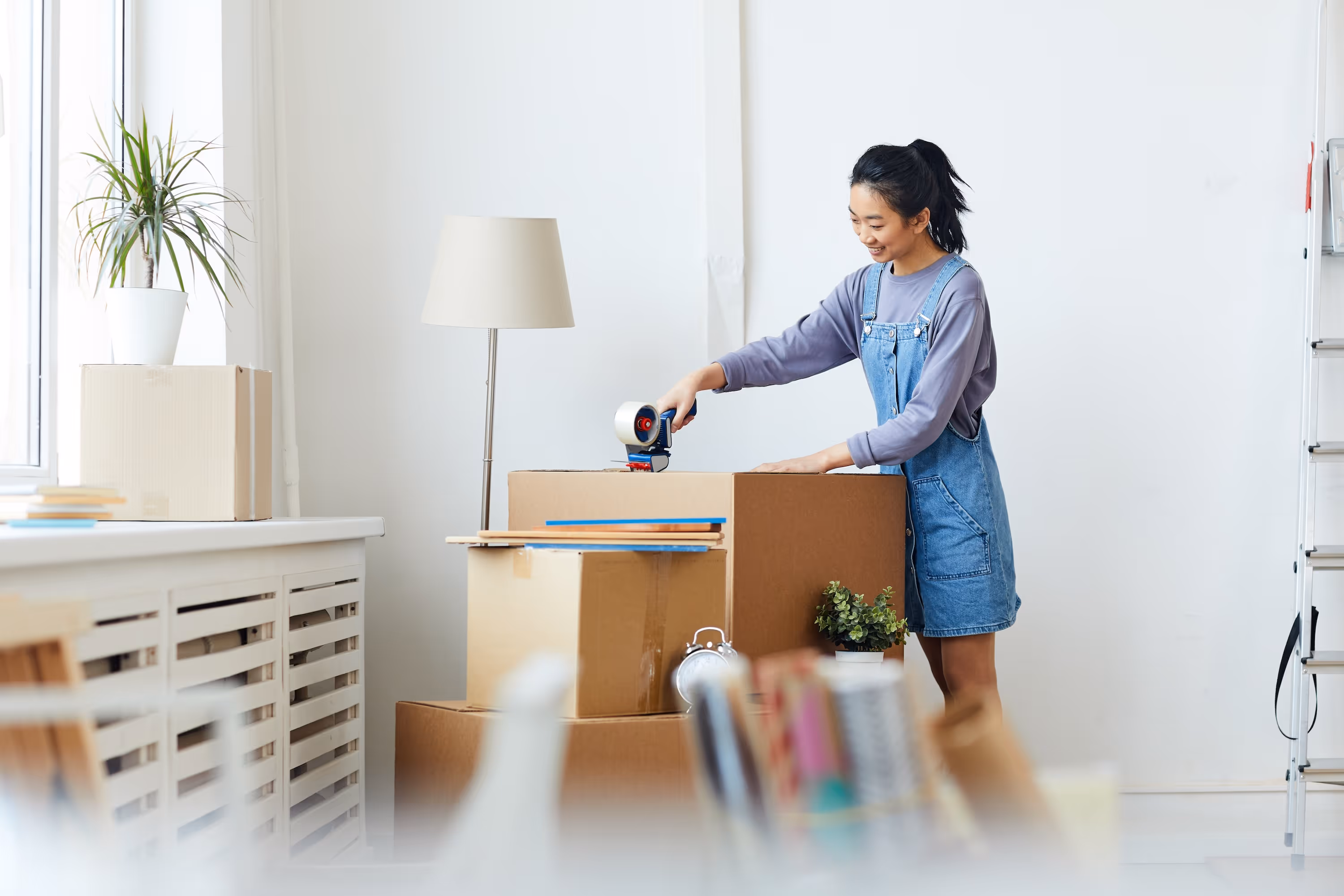 A smiling female student packing or unpacking moving boxes in her bright, modern apartment, showcasing the convenience of moving in at ArtHaus Dwight in Berkeley, CA.