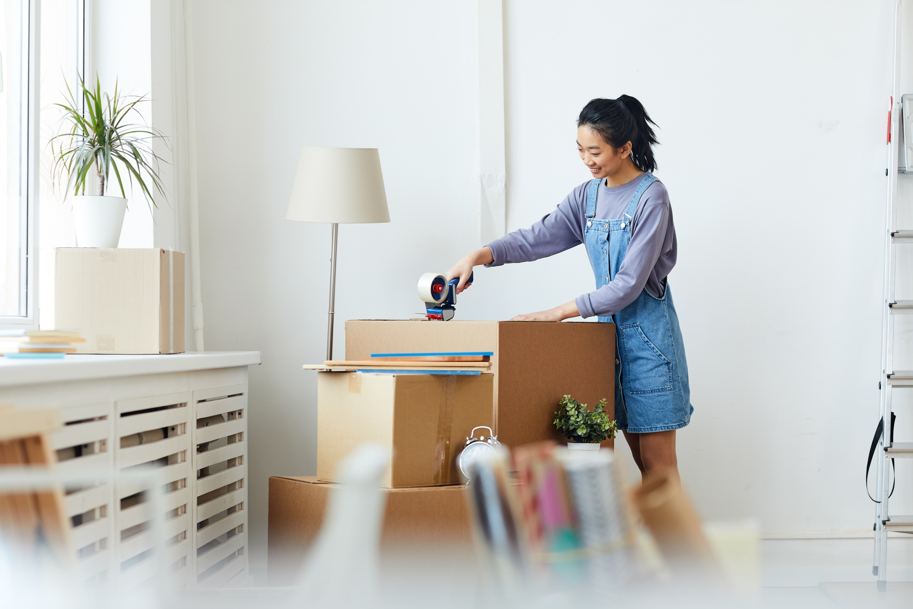 A smiling female student packing or unpacking moving boxes in her bright, modern apartment, showcasing the convenience of moving in at ArtHaus Dwight in Berkeley, CA.