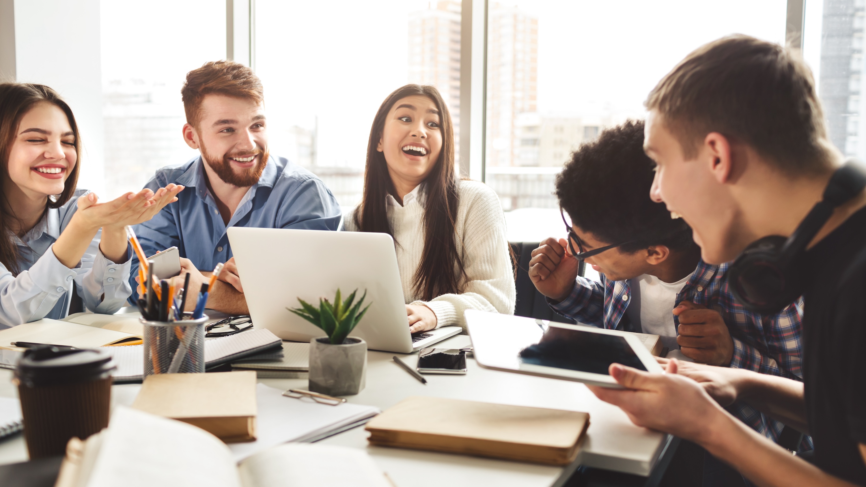 A group of residents laughing and working together with laptops and tablets in a bright, modern community lounge at ArtHaus Dwight, highlighting collaborative workspaces and social resident amenities.