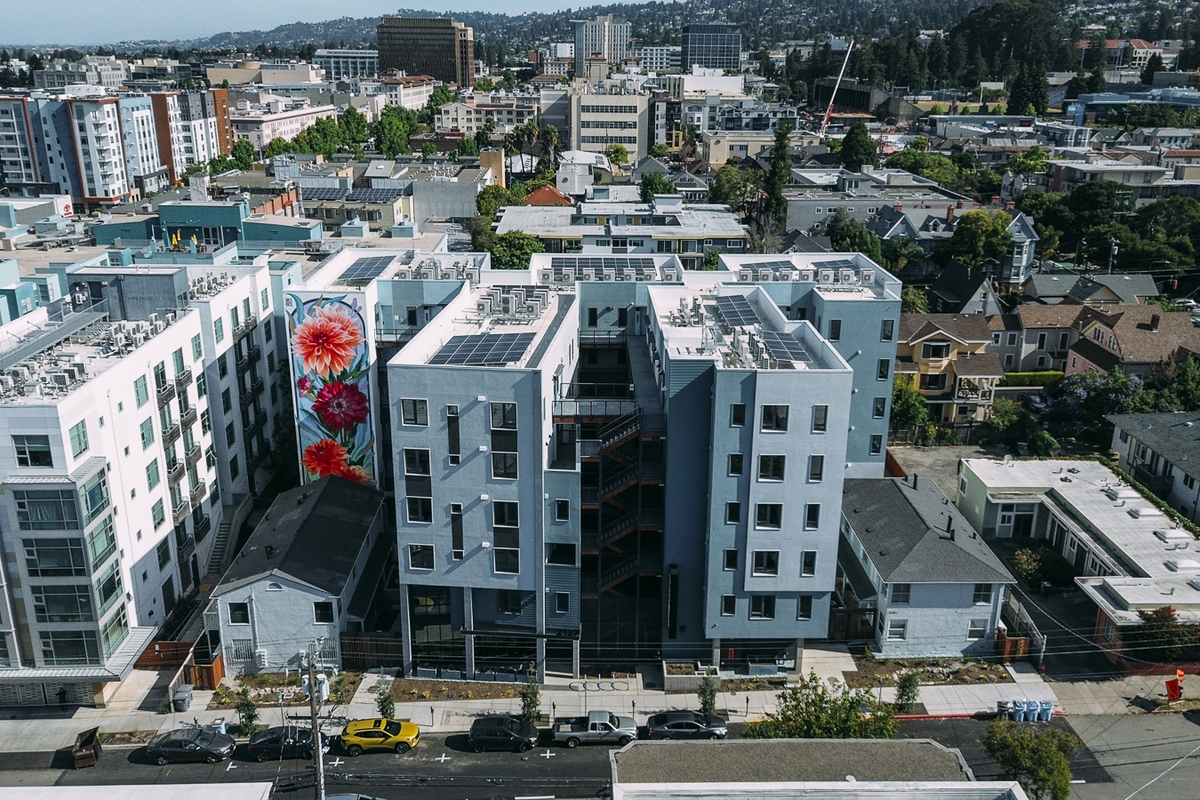 The exterior of ArtHaus Dwight, a multi-story modern apartment building with beige and blue siding, a central staircase, and a large, colorful floral mural on the left side.