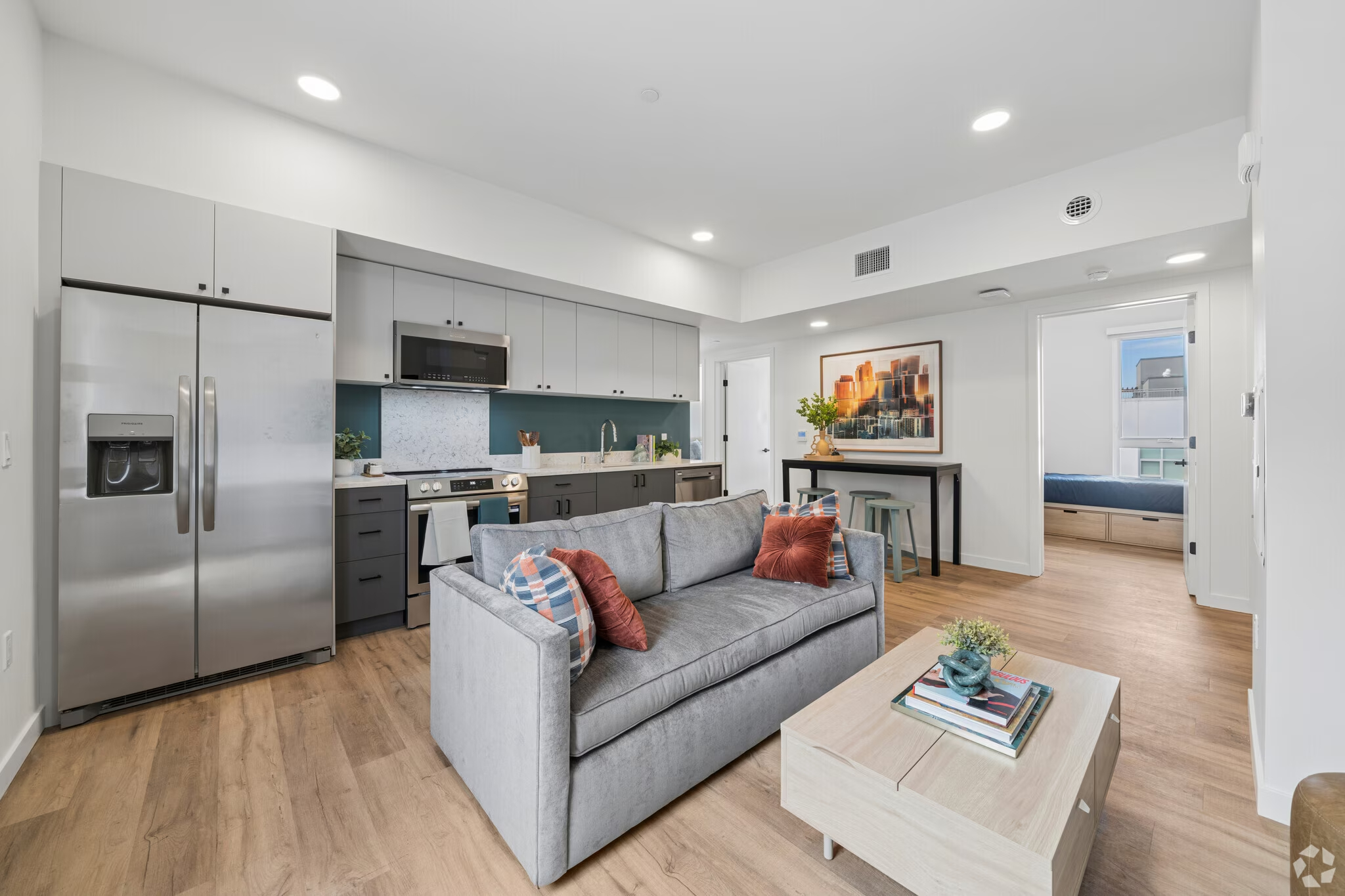 Apartment living room and kitchen featuring a brown leather sofa, wood coffee table, and open-concept layout with stainless steel appliances at ArtHaus Dwight in Berkeley, CA.