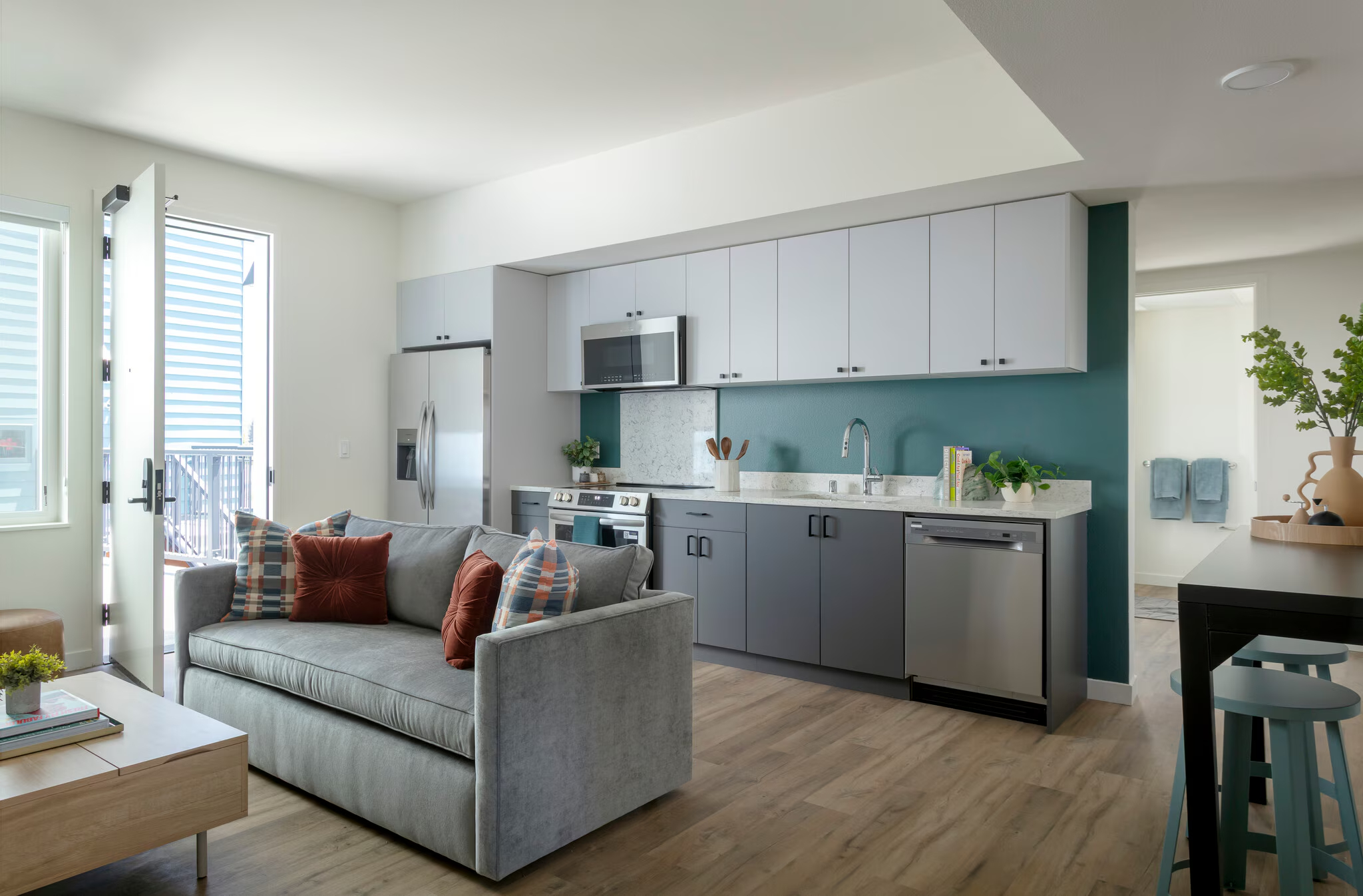 Modern apartment kitchen with two-tone cabinetry (green base, white upper), stainless steel appliances, and a leather sofa in the adjacent living area at ArtHaus Dwight in Berkeley, CA.