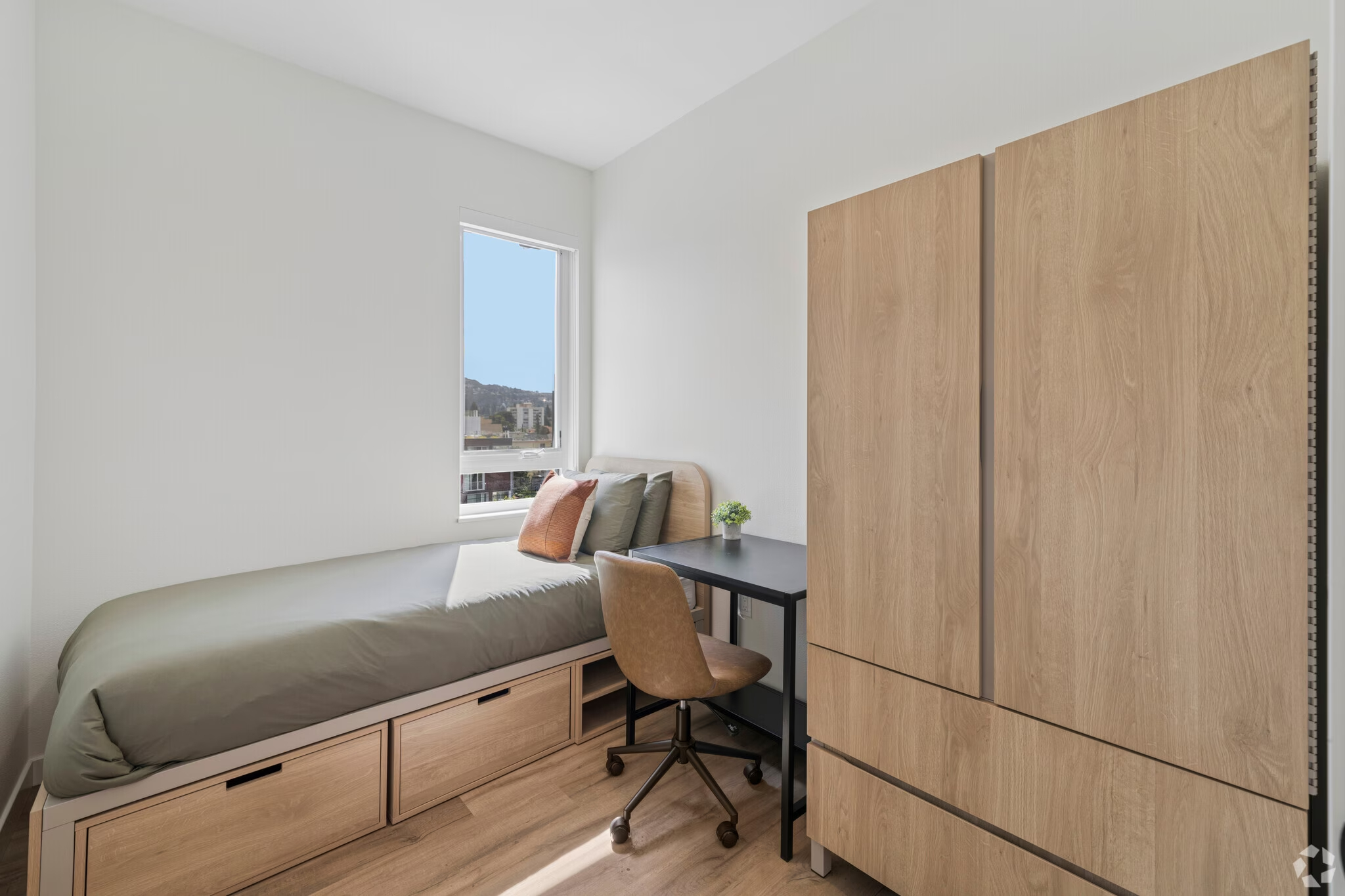 Fully furnished apartment bedroom featuring a bed with under-bed storage, a desk/workspace area, and light wood furnishings at ArtHaus Dwight in Berkeley, CA.
