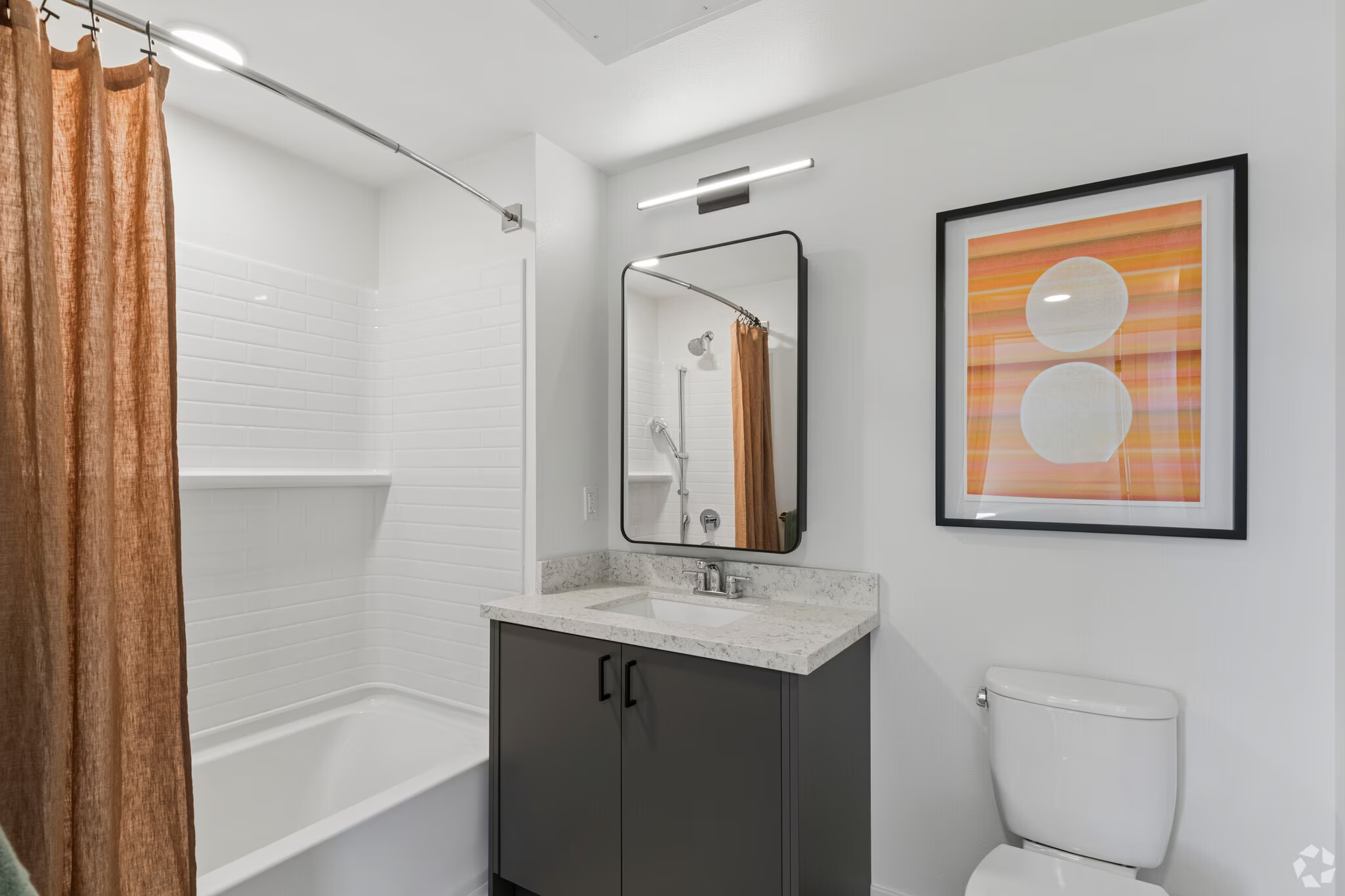Apartment bathroom featuring a vanity with blue cabinetry, a toilet, and a shower/tub with floor-to-ceiling white tile at ArtHaus Dwight in Berkeley, CA.
