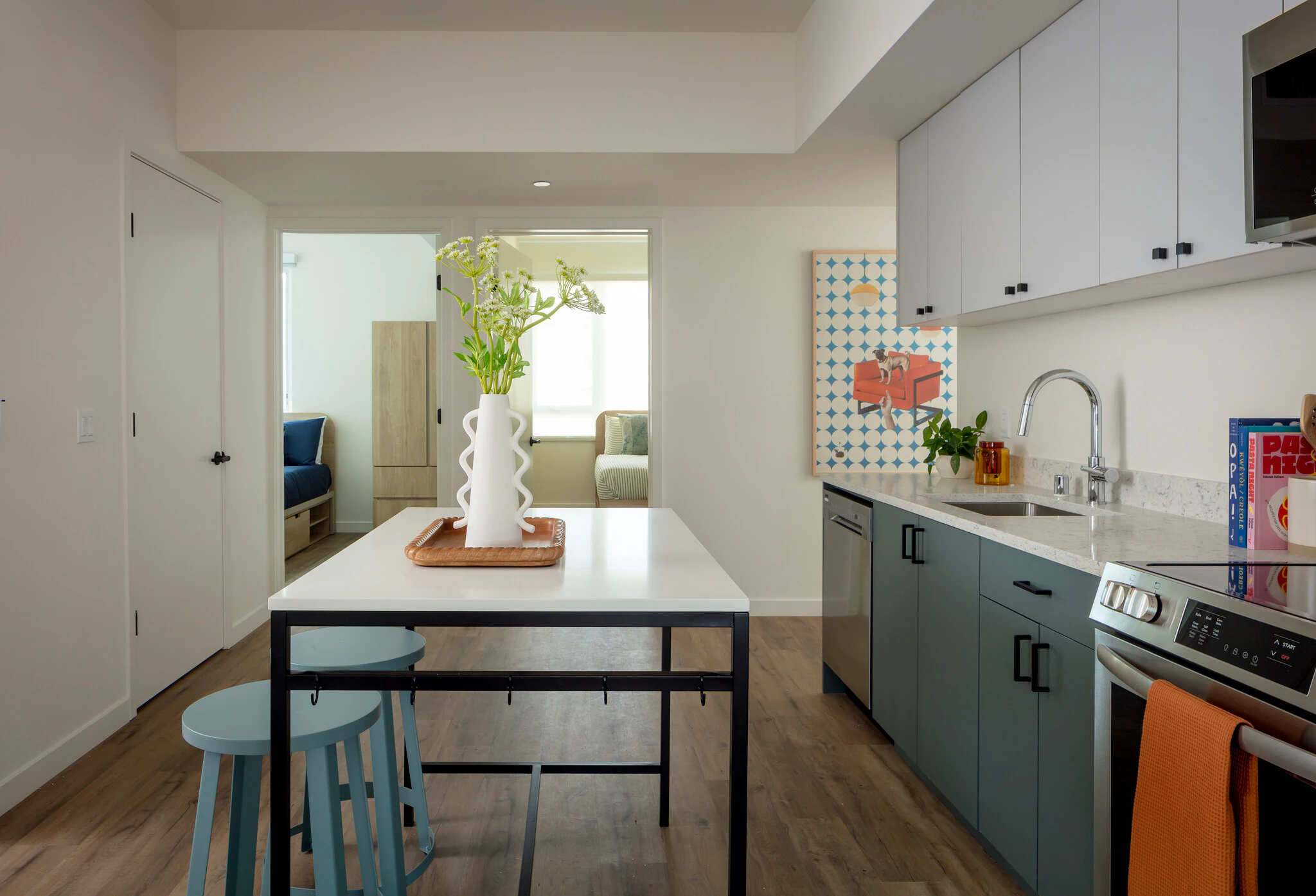 Apartment living room and kitchen featuring a gray sofa, wood coffee table, and open-concept layout with dining area with table and chairs and stainless steel appliances at ArtHaus Dwight in Berkeley, CA.