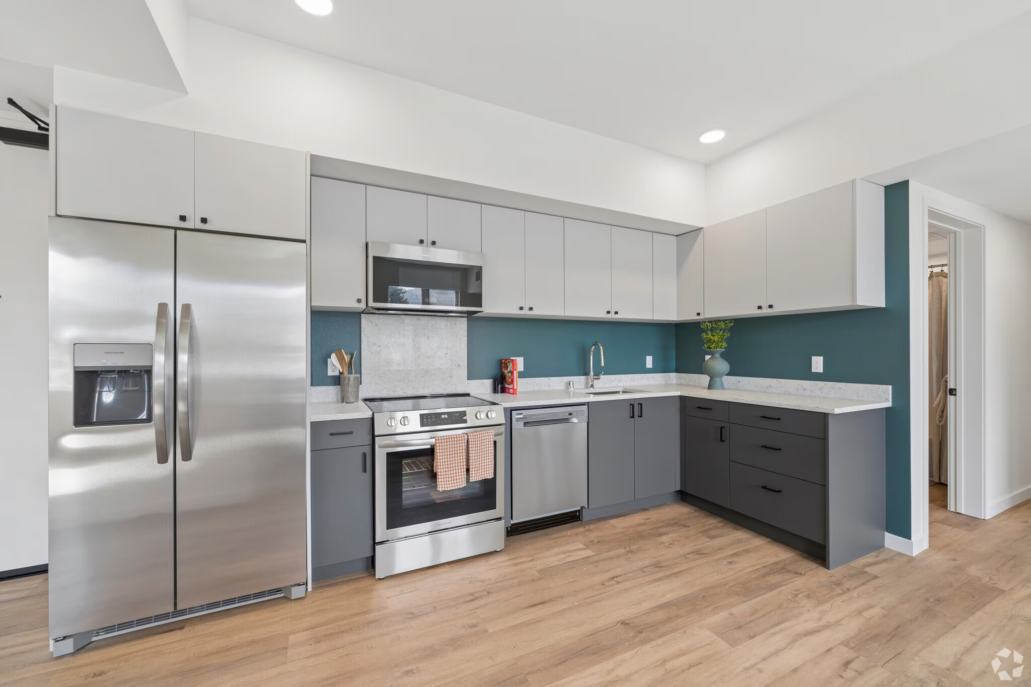 Modern apartment kitchen with two-tone cabinetry (green base, white upper), stainless steel appliances, and a leather sofa in the adjacent living area at ArtHaus Dwight in Berkeley, CA.