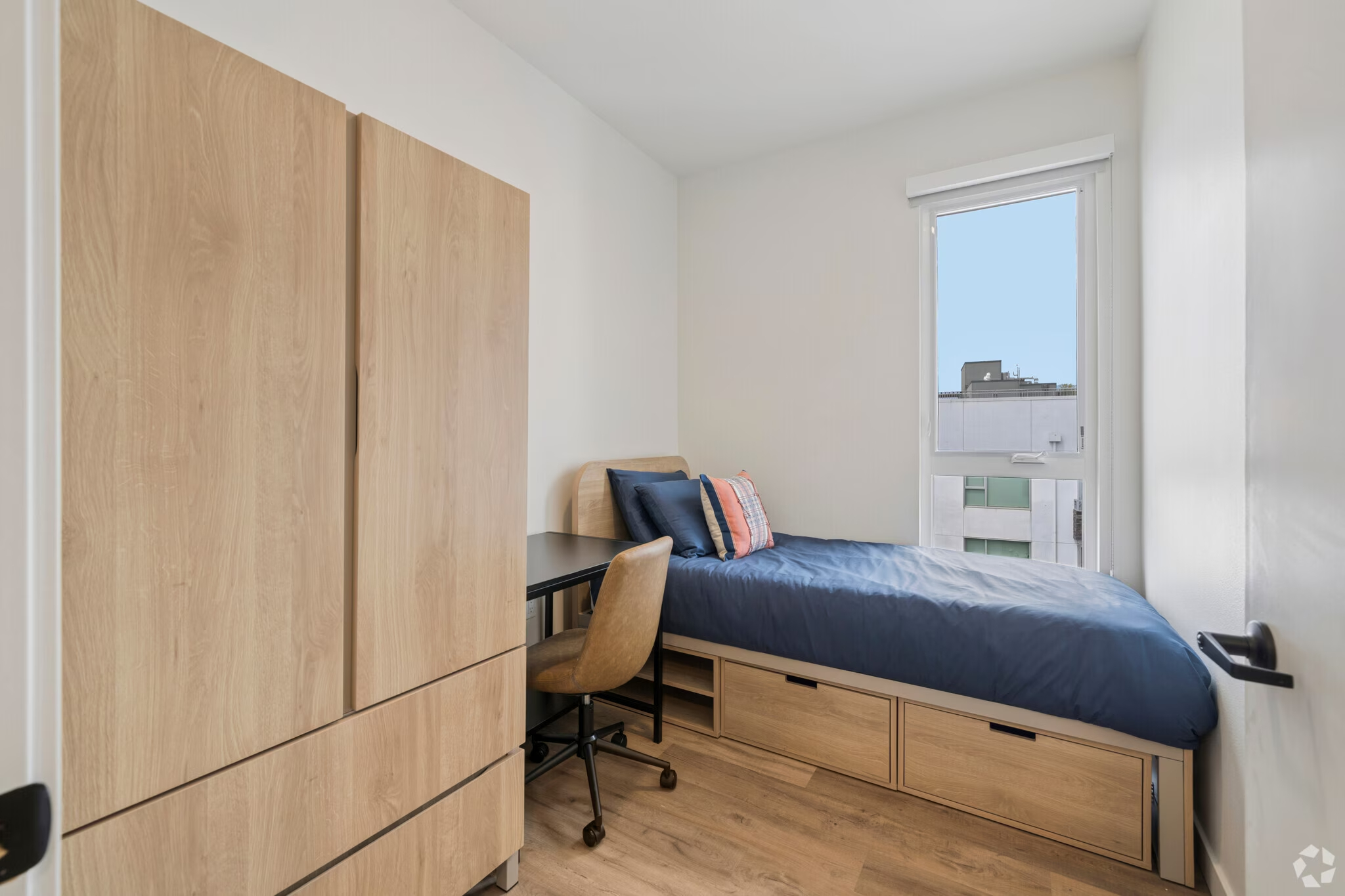 Fully furnished apartment bedroom featuring a bed, a dedicated desk area, and large windows at ArtHaus Dwight in Berkeley, CA.