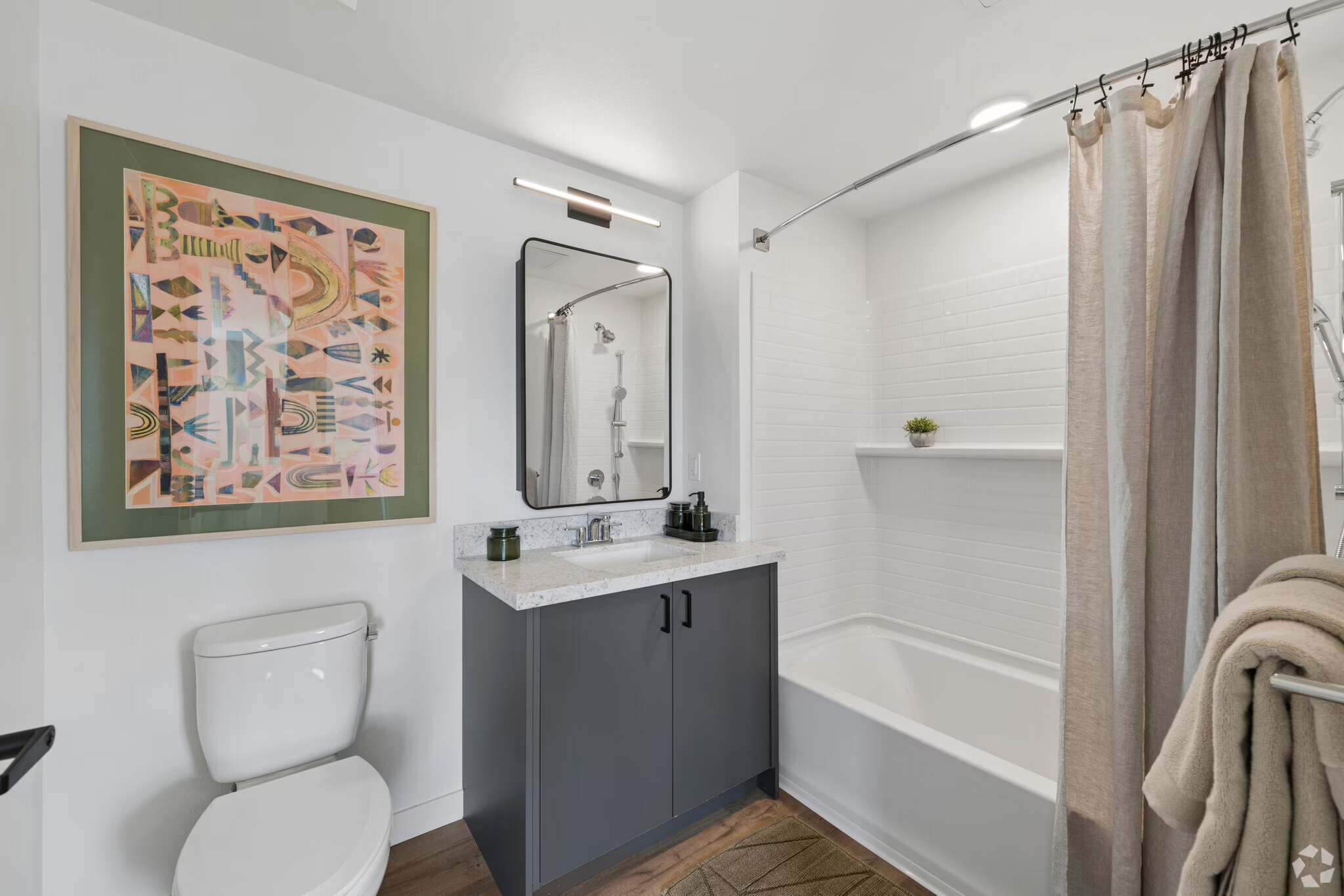 Apartment bathroom featuring a vanity with blue cabinetry, a toilet, and a shower/tub with floor-to-ceiling white tile at ArtHaus Dwight in Berkeley, CA.