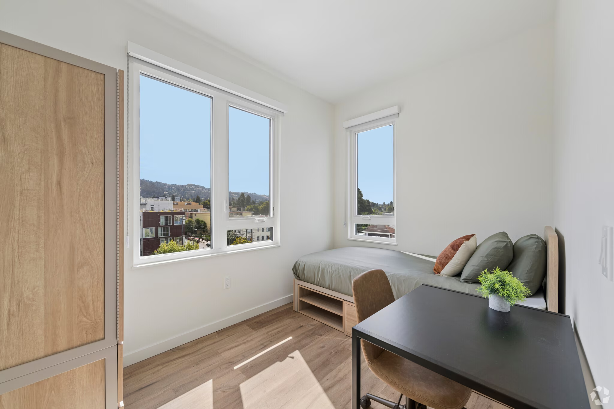 Fully furnished apartment bedroom featuring a bed, a dedicated desk area, and large window at ArtHaus Dwight in Berkeley, CA.