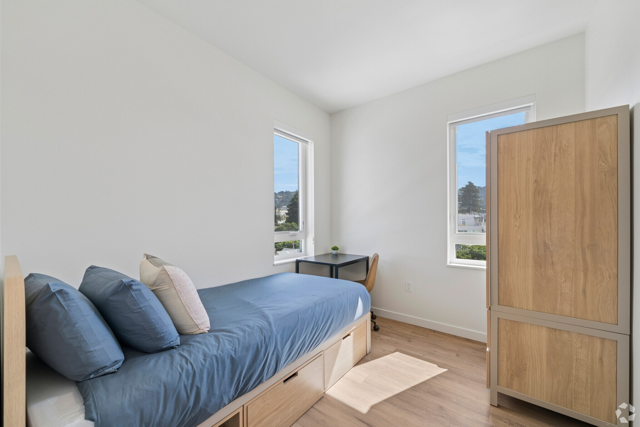 Fully furnished apartment bedroom featuring a bed, a dedicated desk area, and large window at ArtHaus Dwight in Berkeley, CA.